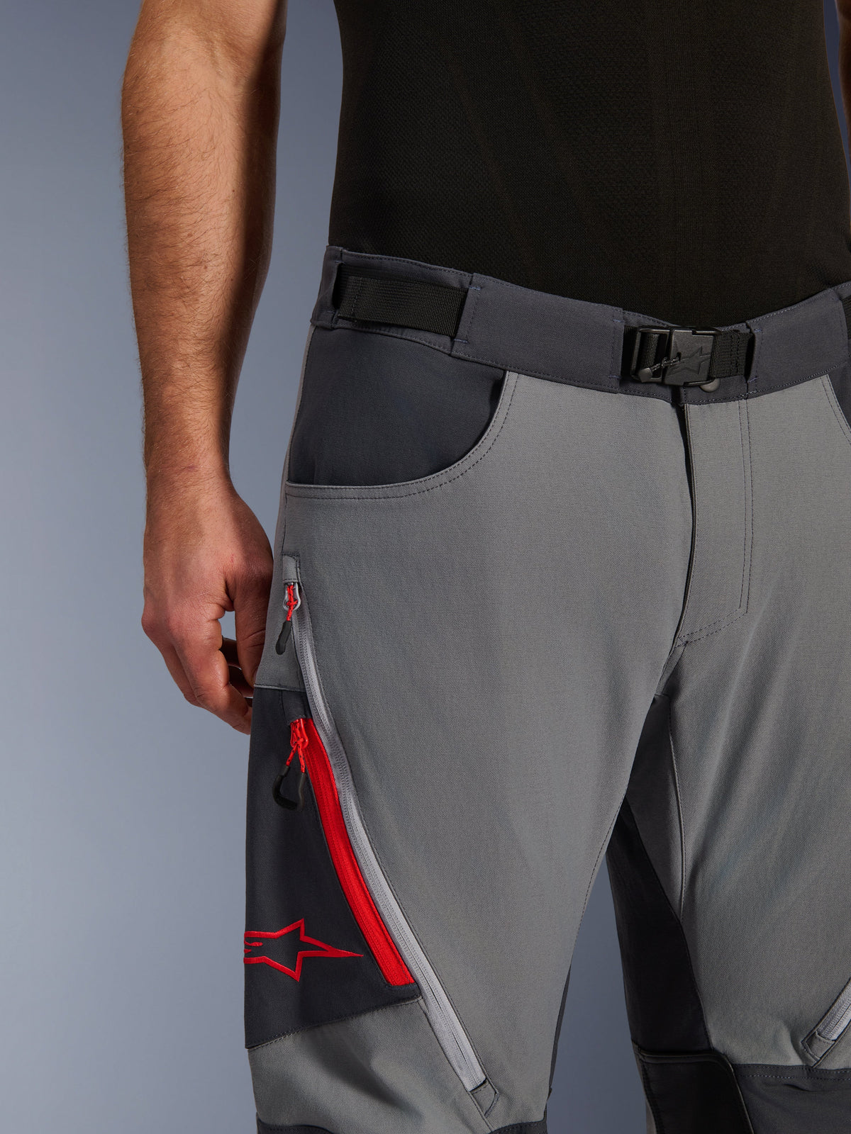 Alpinestars Maxdura Dual Pants, spodnie motocyklowe adventure, ciemnoszare i głęboko szare, zbliżenie na regulowany pasek w talii z klamrą magnetyczną, kieszeń cargo na zamek z czerwonymi detalami i logo Alpinestars