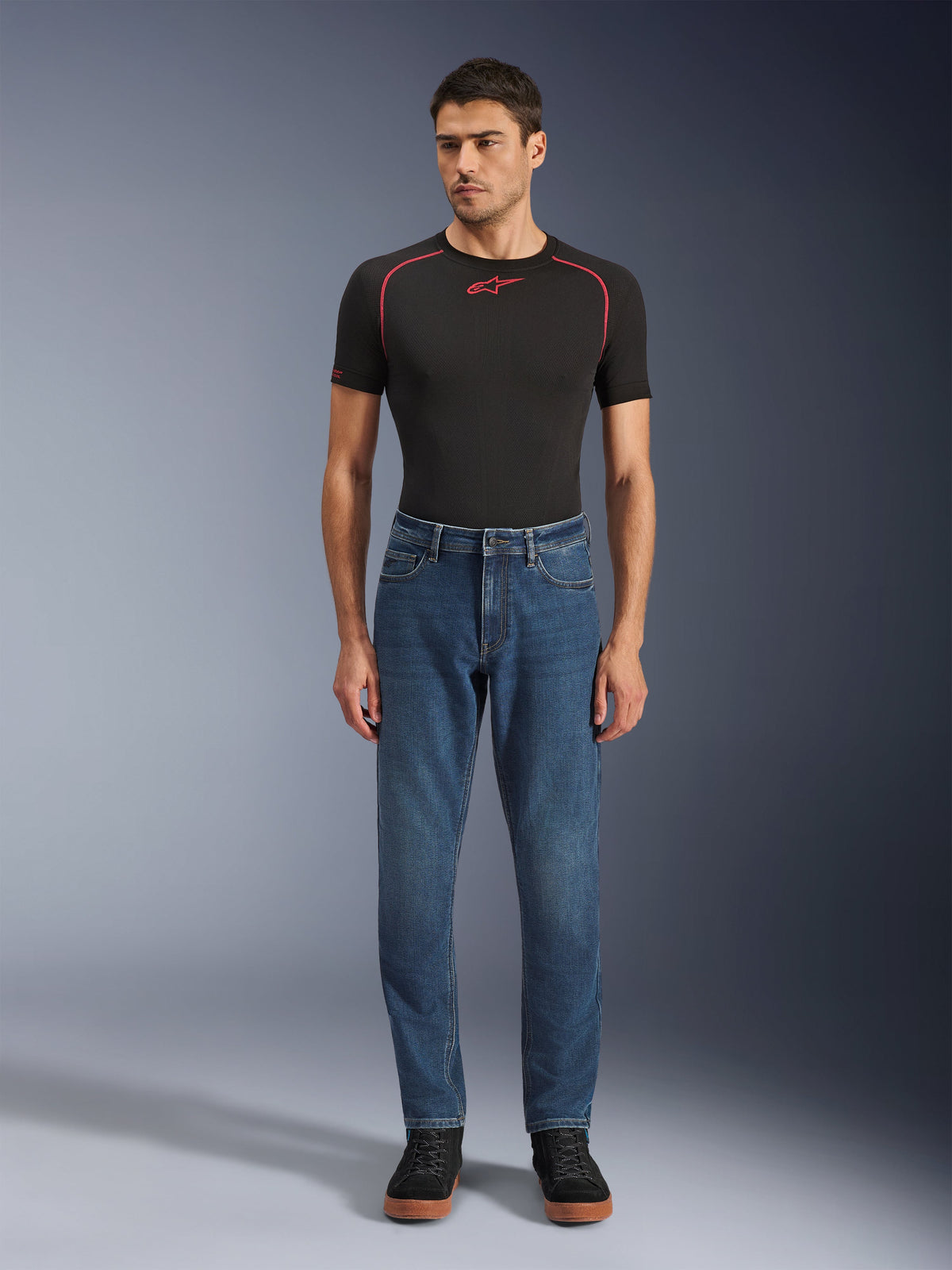 Alpinestars Flex-AST 5 Denim Pants, Indigo Washed blue denim motorcycle pants, regular tapered fit, worn by a model with a black Alpinestars base layer and black casual shoes, urban riding lifestyle apparel.