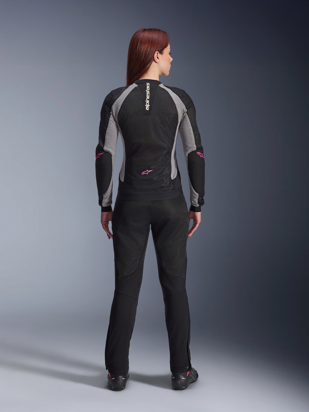 Damskie spodnie Alpinestars Stella Troop-Air w kolorze czarnym, widok z tyłu, zestawione z czarno-szarą meshową kurtką motocyklową z różowymi akcentami, zdjęcie studyjne prezentujące techniczną, wentylowaną konstrukcję tekstylną.