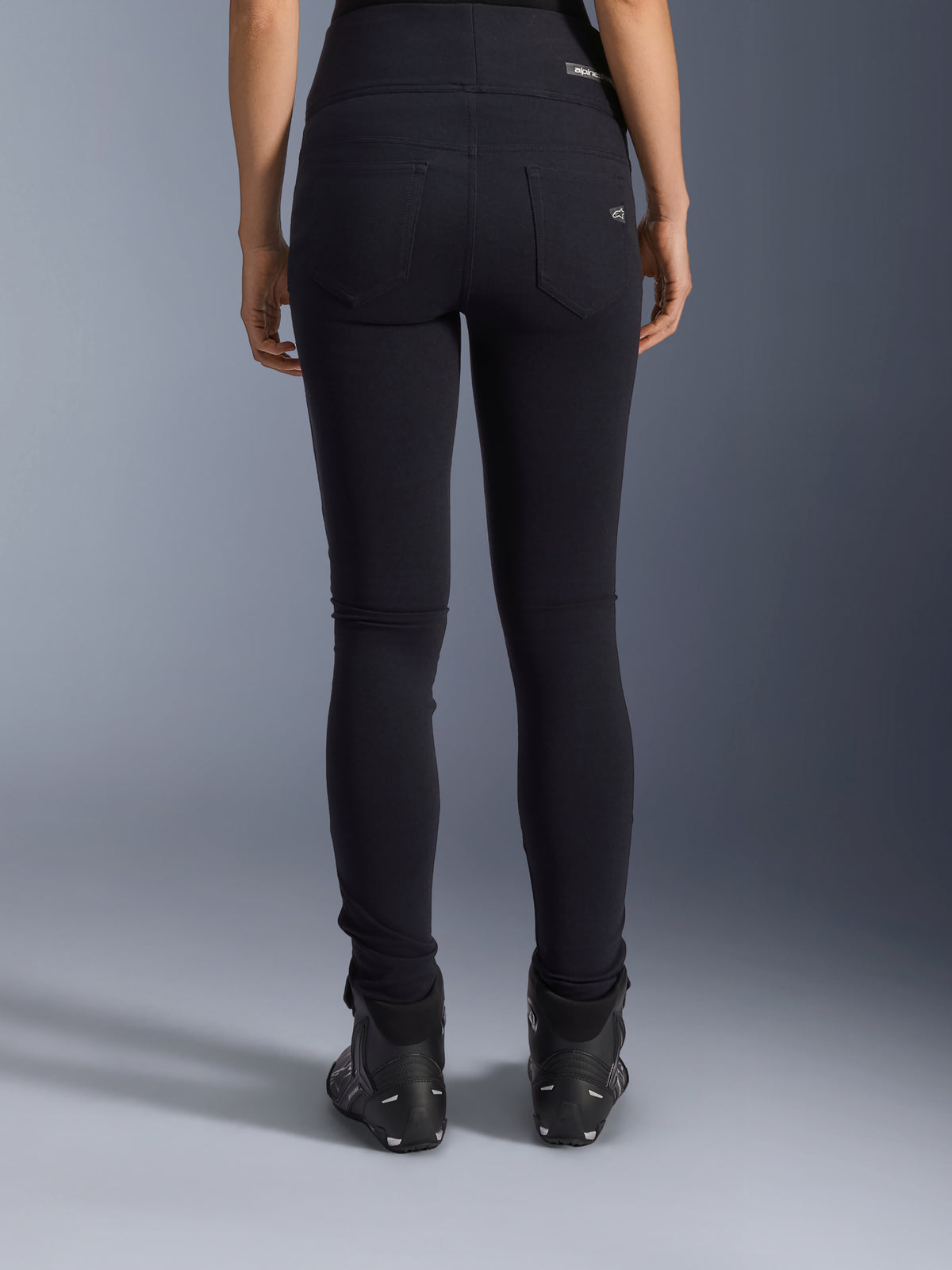 Legginsy Alpinestars Stella Flex-Ast, damskie legginsy motocyklowe, czarne, widok z tyłu ukazujący tylne kieszenie i dopasowany krój, noszone z czarnymi butami motocyklowymi, miejski styl jazdy
