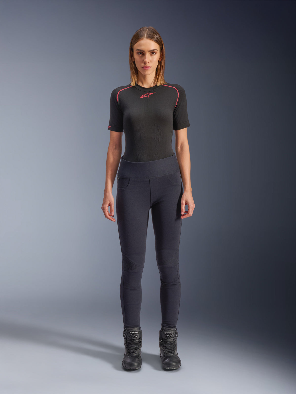 Alpinestars Stella Flex-Ast Leggings, damskie legginsy motocyklowe, czarne, noszone z czarnym topem z krótkim rękawem z czerwonymi detalami i czarnymi butami motocyklowymi, dopasowana współczesna miejska odzież motocyklowa, widok z przodu