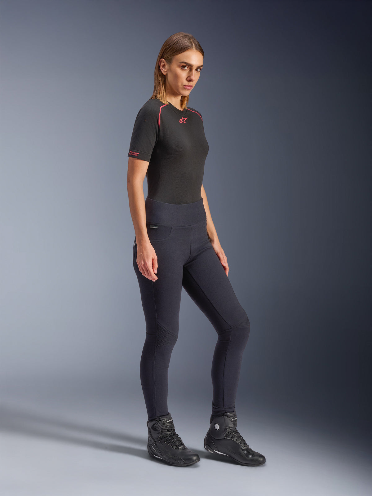 Alpinestars Stella Flex-Ast Leggings, damskie legginsy motocyklowe w kolorze czarnym, dopasowany krój z wysokim stanem, prezentowane z czarnym t-shirtem z czerwonymi akcentami i czarnymi butami motocyklowymi, ujęcie całej sylwetki w studiu