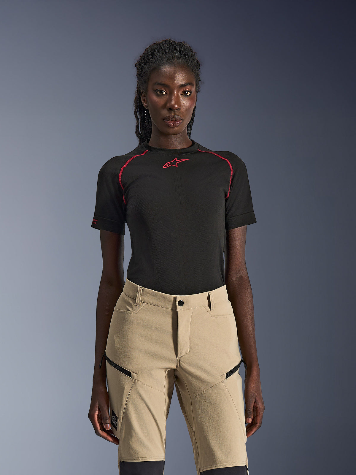 Spodnie Alpinestars Stella Flex-AST Explorer, damskie spodnie motocyklowe w kolorze piaskowym, noszone z czarną techniczną koszulką z krótkim rękawem z czerwonymi szwami, odzież typu adventure touring z zapinanymi na zamek kieszeniami cargo i wytrzymałym materiałem ripstop