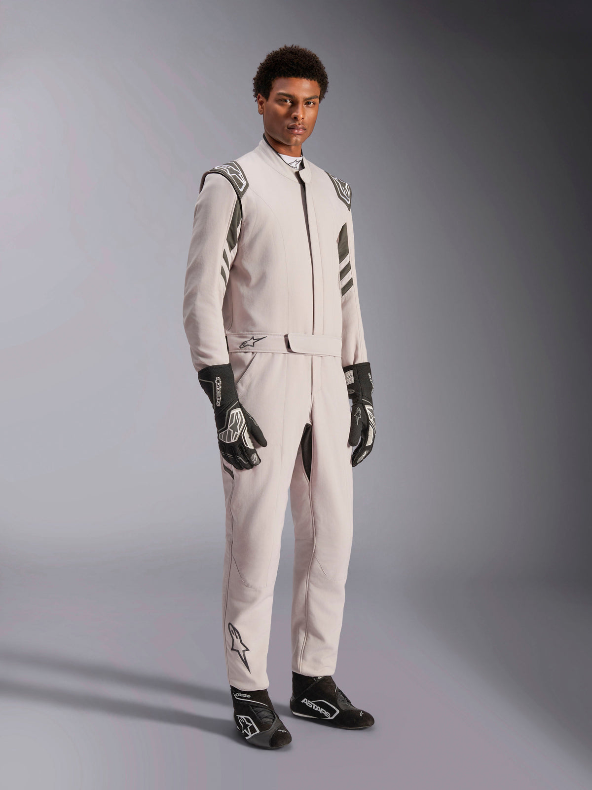 Alpinestars GP Race V3 Suit FIA, kombinezon wyścigowy w kolorze Silver Anthracite, jednoczęściowy strój kierowcy z pagonami na ramionach i pasem w talii, zestawiony z czarno-białymi rękawicami i butami wyścigowymi, elegancki design do profesjonalnych wyścigów samochodowych