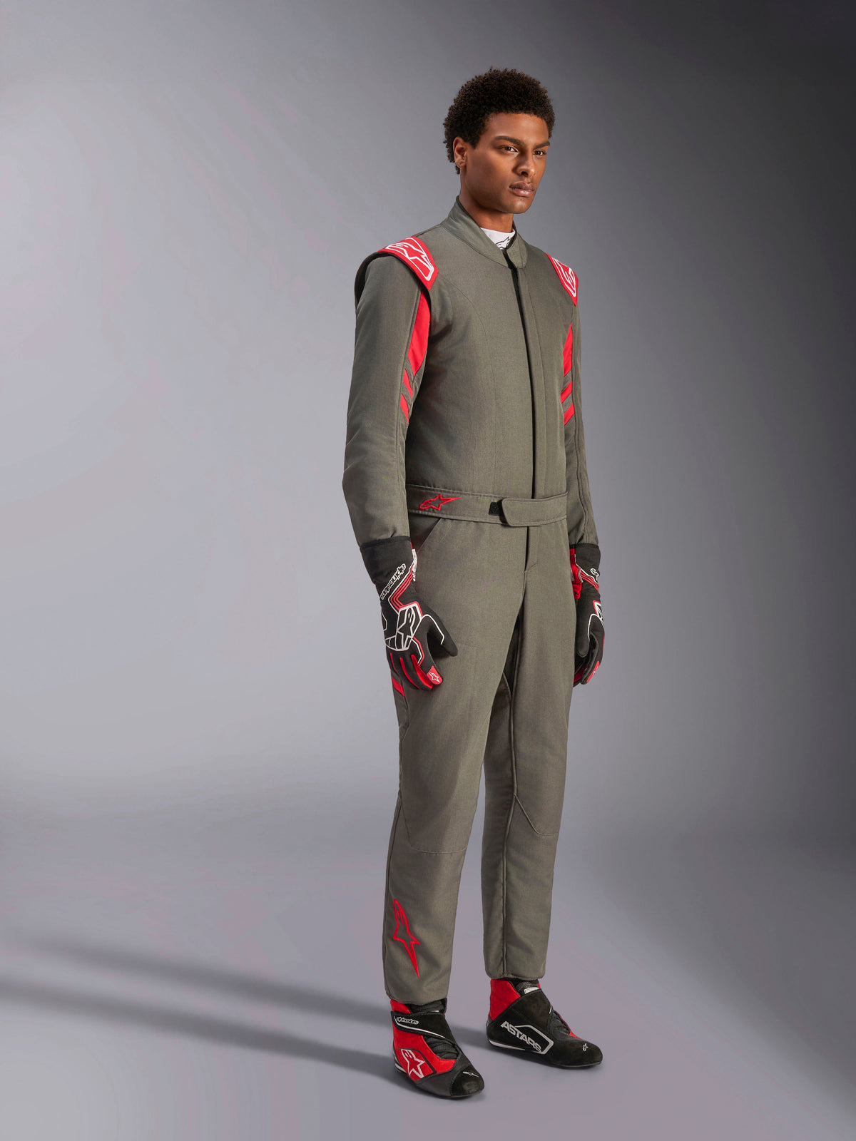 Alpinestars GP Race V3 Suit FIA, antracytowo-czerwony kombinezon wyścigowy, zestawiony z dopasowanymi rękawicami i butami wyścigowymi, z czerwonymi epoletami na ramionach i brandingiem, smukła dwuwarstwowa konstrukcja techniczna do sportów motorowych