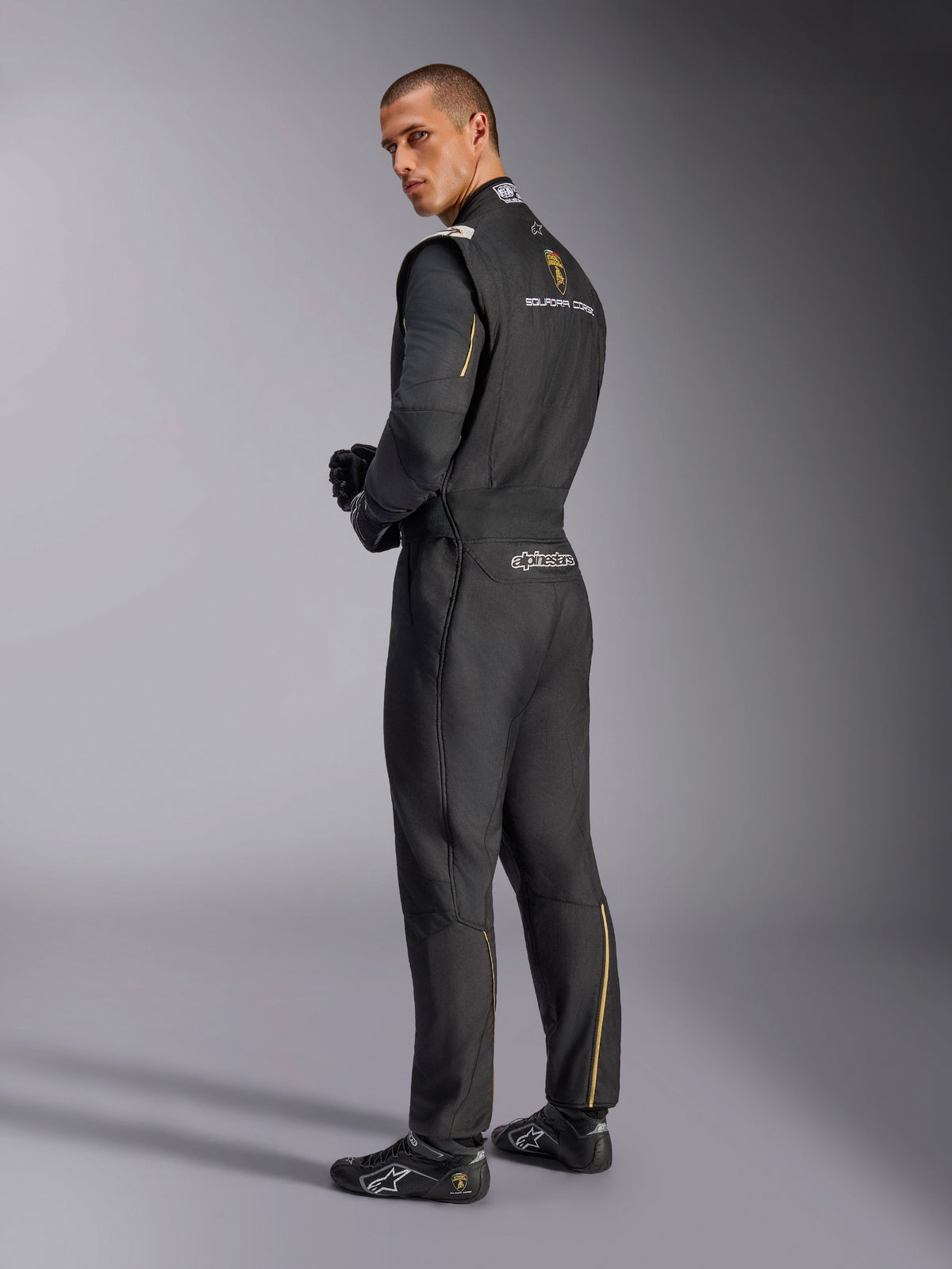Alpinestars Limited Edition Lamborghini GP Tech V4 Suit, Professional Auto Racing Suit, Black with Silver and Gold accents, back view showing Lamborghini Squadra Corse and Alpinestars branding, worn with black racing gloves and footwear, sleek motorsport design