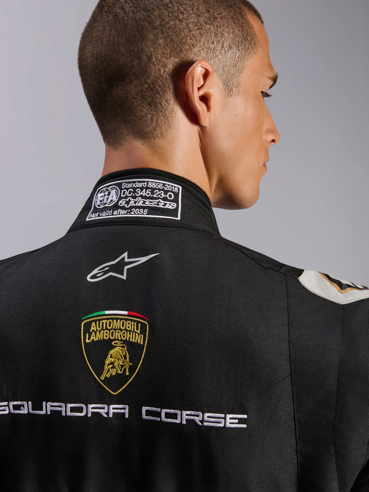 Alpinestars Limited Edition Lamborghini GP Tech V4 Suit FIA, close-up of the upper back and collar, black suit featuring the Automobili Lamborghini shield and Squadra Corse embroidery, Alpinestars logo, and FIA 8856-2018 certification label on the neckline.
