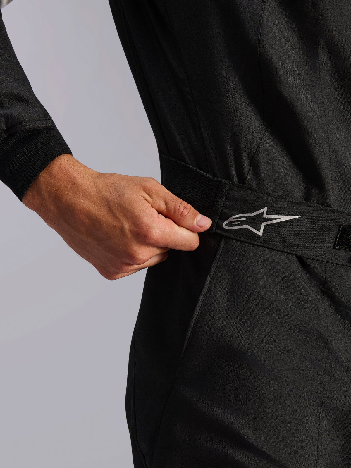 Alpinestars Limited Edition Lamborghini GP Tech V4 Suit FIA, Auto Racing Suit, Black, close-up of the elasticated waist construction being adjusted by hand for a cinch fit, featuring a silver Alpinestars logo on the belt