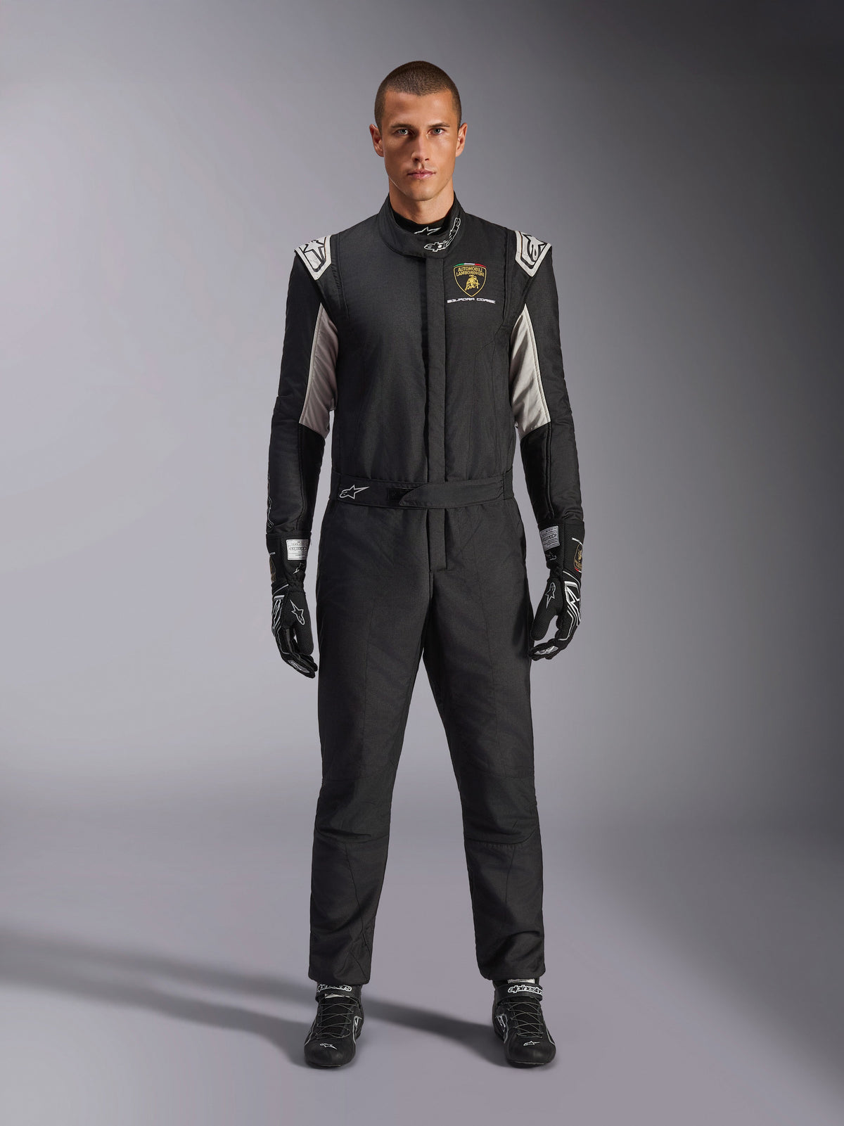 Alpinestars Limited Edition Lamborghini GP Tech V4 Suit FIA, professional auto racing suit, Black with Silver and Gold accents, featuring Automobili Lamborghini Squadra Corse logo on chest, worn with matching racing gloves and boots, sleek athletic design for circuit competition
