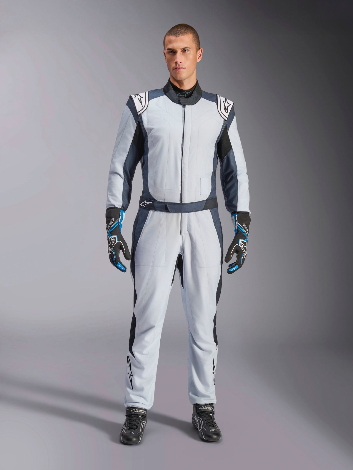 Alpinestars GP Pro Comp V2 - FIA, srebrno-niebieski i szary samochodowy kombinezon wyścigowy, certyfikat FIA, na modelu.