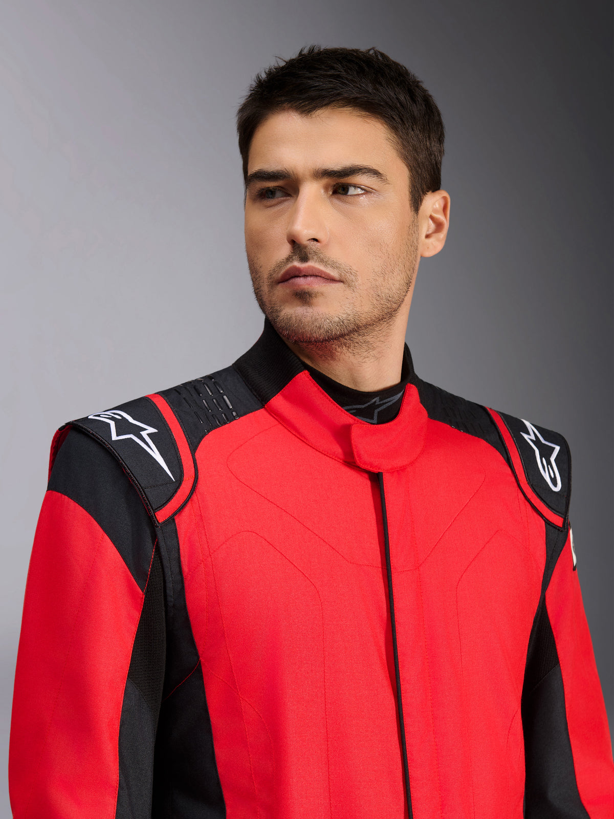 Male model wearing Alpinestars GP Pro Comp V2 FIA Auto Racing Suit, Red and Black, featuring white Astars logos on shoulders and silicon grip technology detailing, professional motorsport apparel