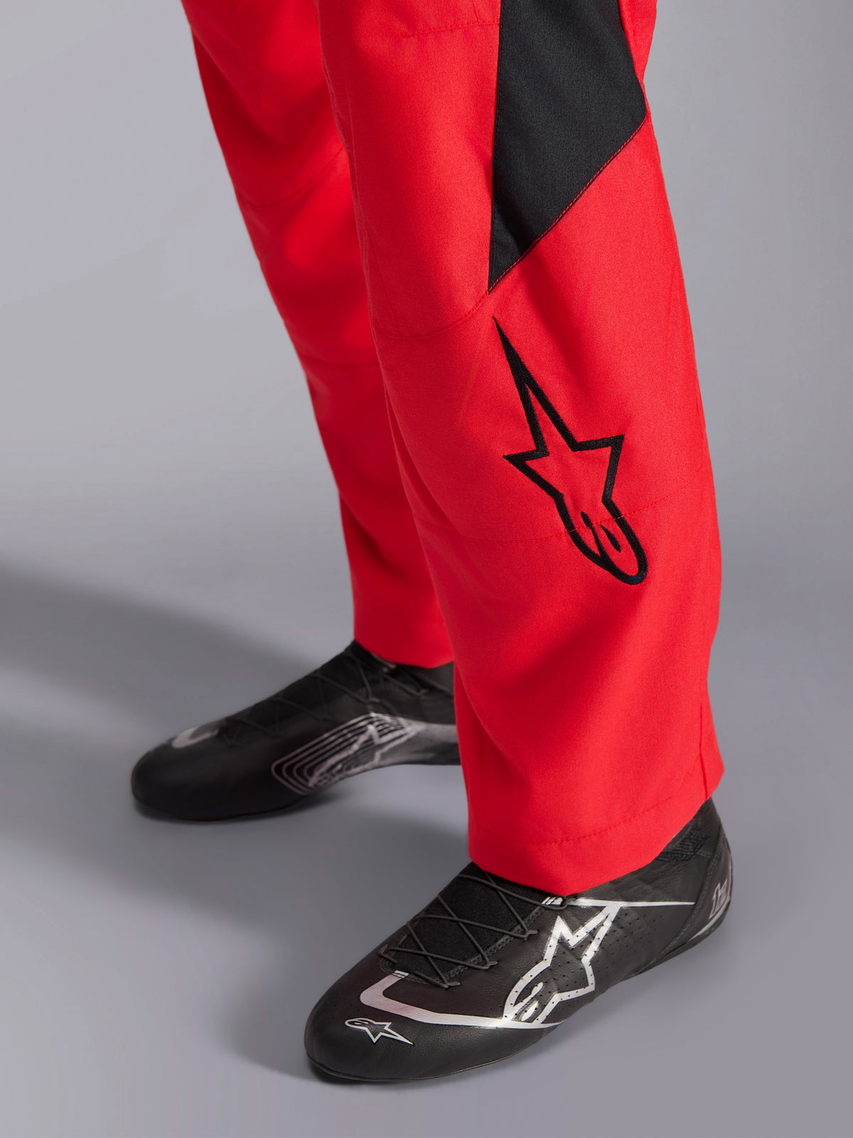 Alpinestars GP Pro Comp V2 FIA Racing Suit, close-up of the lower leg and racing shoes, Red with a black Astars logo and panel, paired with black performance racing footwear, auto racing gear.