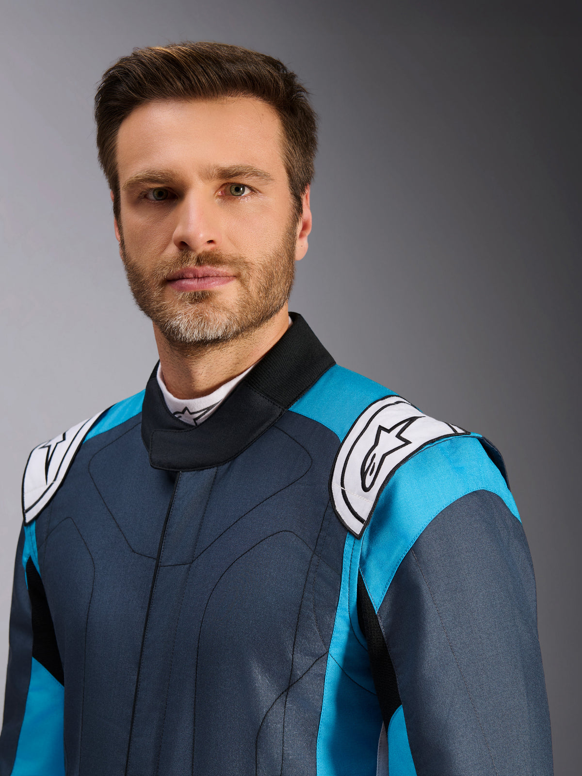 Alpinestars GP Pro Comp V2 FIA Suit in Asphalt Cyan White, professional men's auto racing gear, on-model close-up.