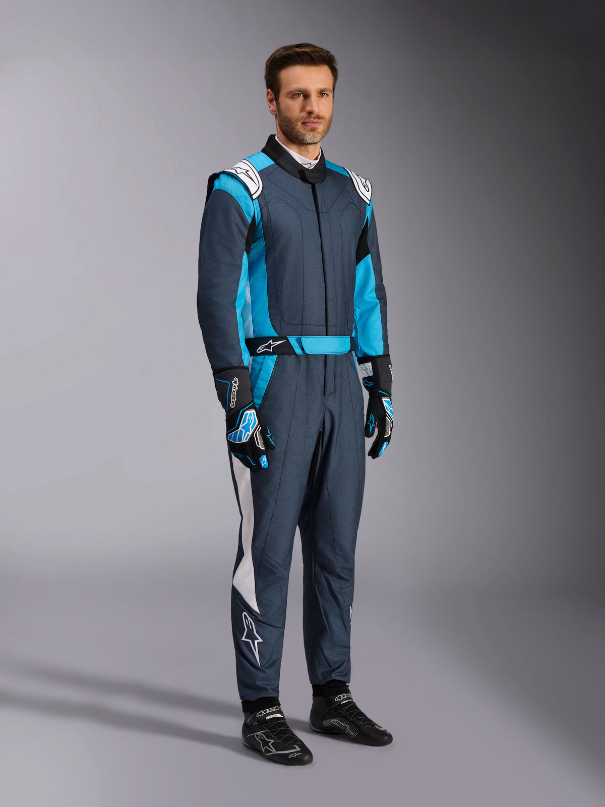 Alpinestars GP Pro Comp V2 FIA Suit, professional auto racing gear in Asphalt and Cyan, worn by a man.
