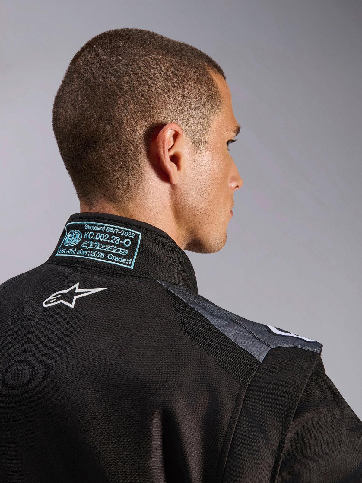 Alpinestars KMX-5 V3 Suit w kolorze czarnym i Dark Shadow, widok z bliska na plecy i kołnierz prezentujący białe logo Astars, metkę certyfikacyjną FIA 8877-2022 Klasa 1 oraz wentylowane panele siatkowe na ramionach.