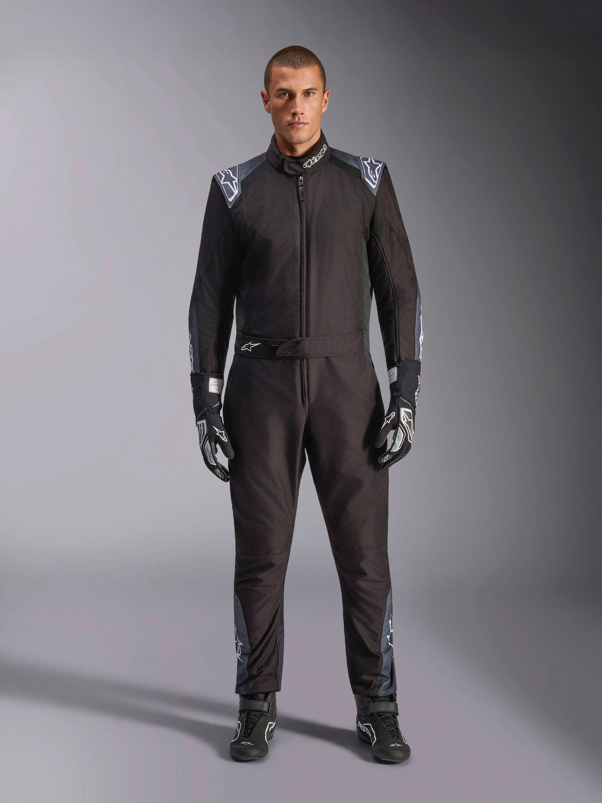 Kombinezon Alpinestars KMX-5 V3, kombinezon kartingowy, kolor Black Dark Shadow, widok całej sylwetki modelu w kombinezonie z pasującymi rękawicami i butami, ciemnoszare akcenty i białe logo Alpinestars na ramionach i pasku, profesjonalny sprzęt wyścigowy