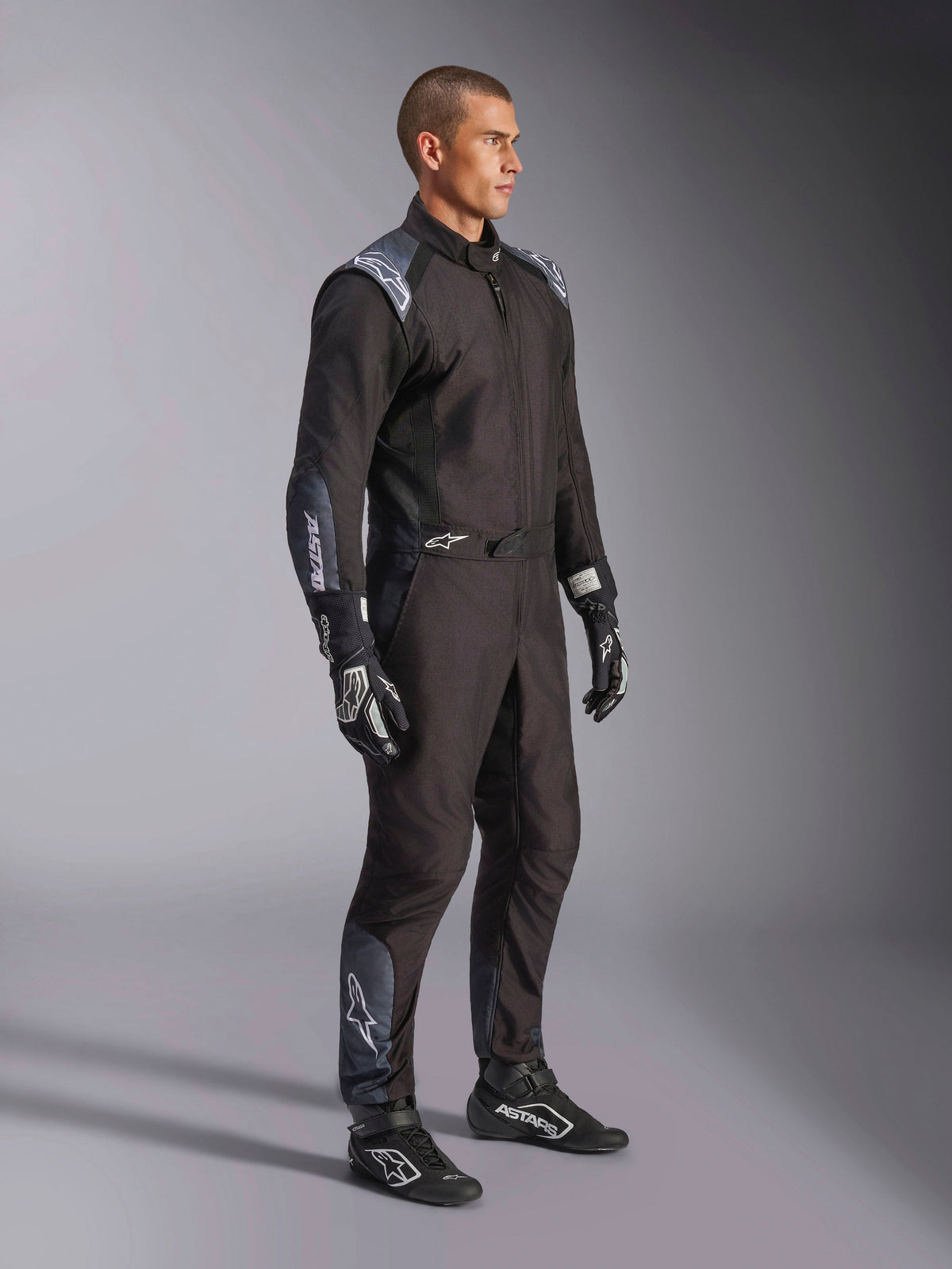 Kombinezon Alpinestars KMX-5 V3, kombinezon kartingowy w kolorze Black Dark Shadow, zestawiony z pasującymi czarnymi rękawicami i butami wyścigowymi, laserowo wycinane perforacje i panele z siatki technicznej, smukła dwuwarstwowa konstrukcja z białym logo dla profesjonalnego motorsportu.