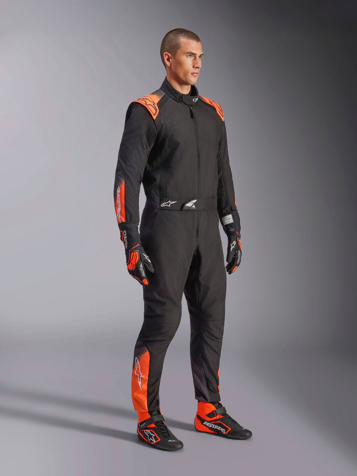 Alpinestars KMX-5 V3, męski jednoczęściowy kombinezon kartingowy, czarny i pomarańczowy fluo, tekstylny, certyfikat FIA klasa 1, noszony przez modela.