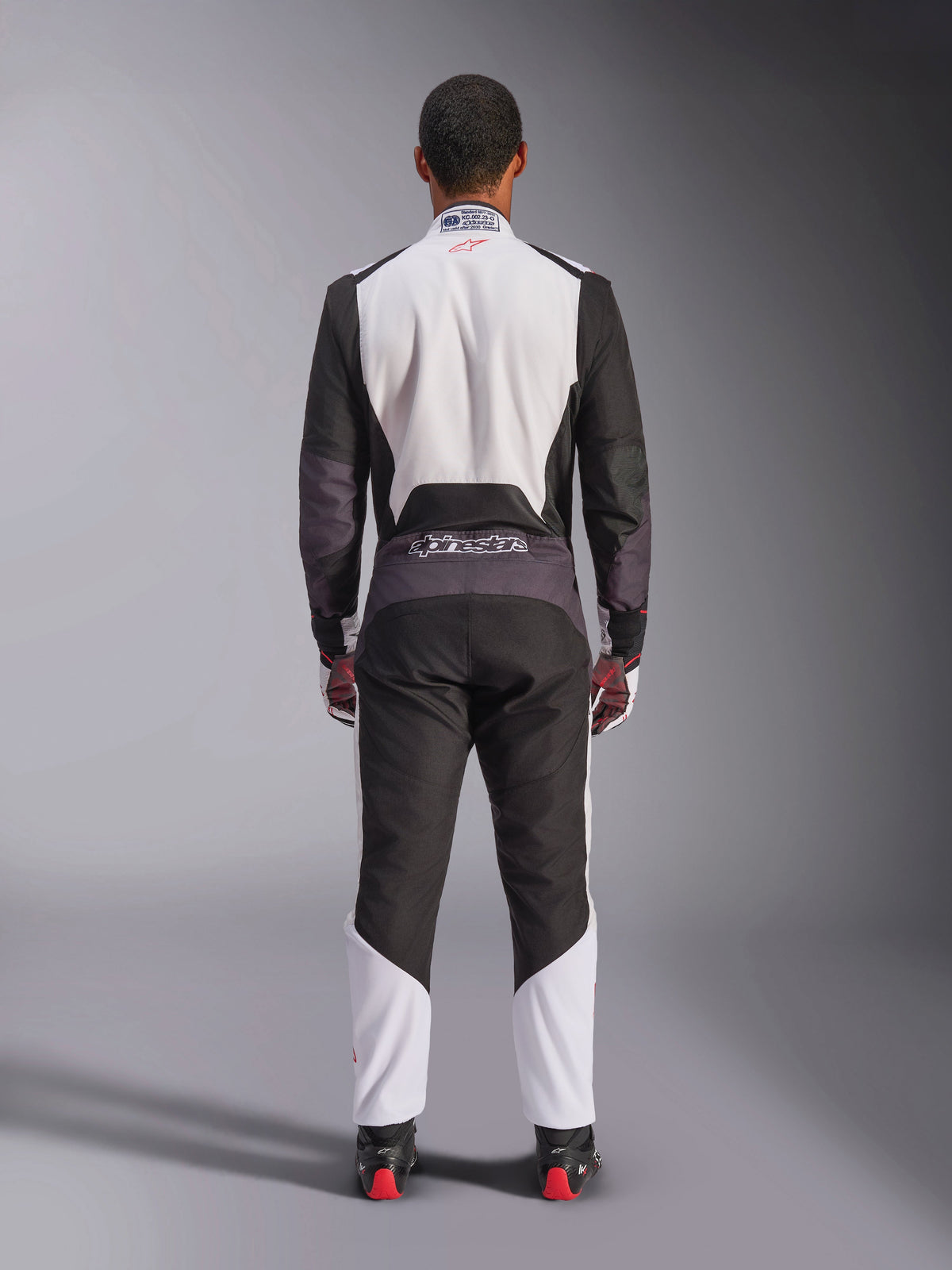 Kombinezon Alpinestars KMX-5 V3, kombinezon kartingowy, biały, czarny i jaskrawoczerwony, widok z tyłu, jednoczęściowy kombinezon wyścigowy z oddychającymi panelami z siatki i logo Alpinestars w pasie, noszony z pasującymi rękawicami i butami wyścigowymi