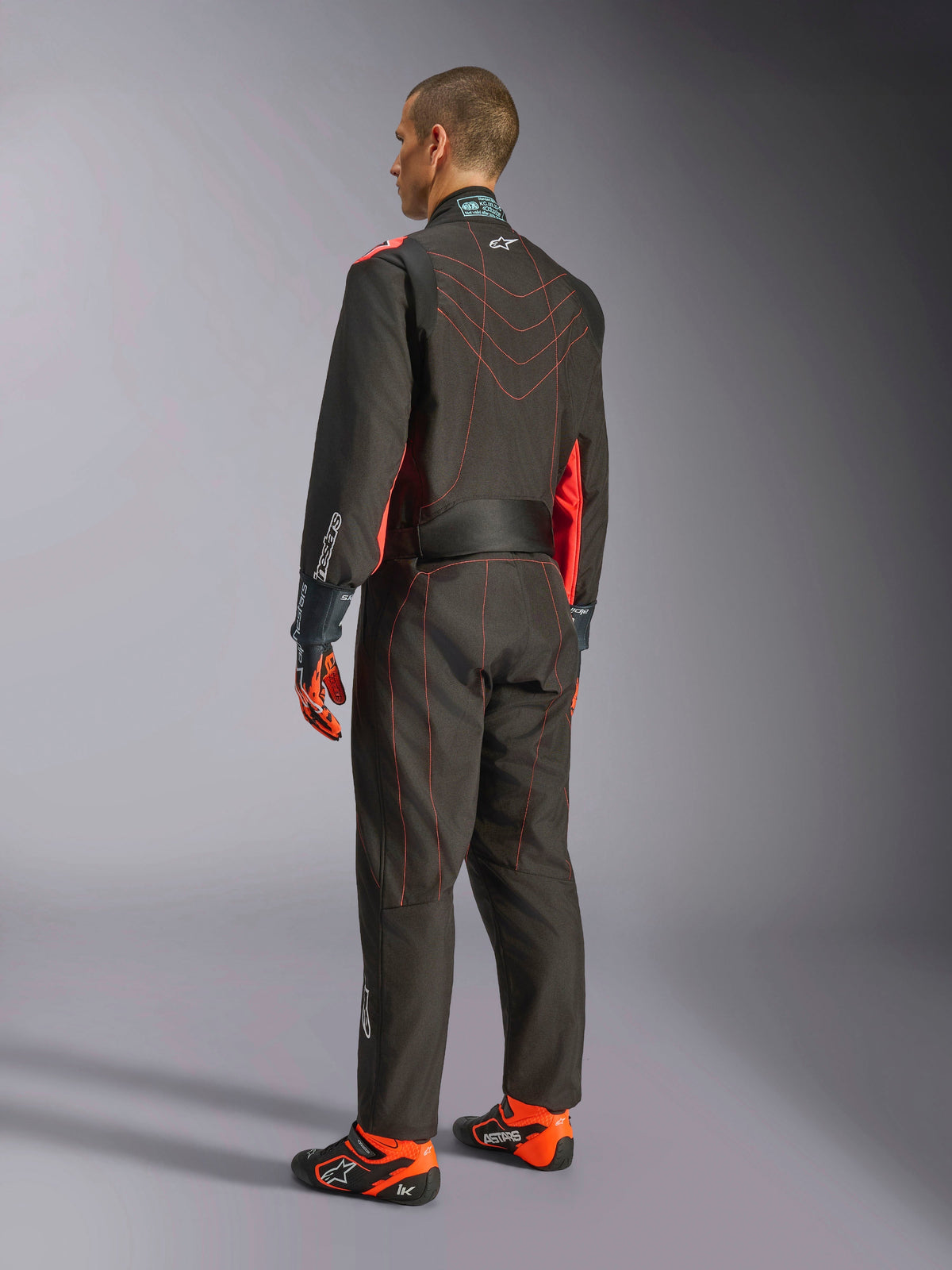 Alpinestars KMX-9 V3 Suit, kombinezon kartingowy, czarny i czerwony fluo, widok z tyłu, z czerwonymi kontrastowymi przeszyciami i fluorescencyjnymi panelami bocznymi, noszony z rękawicami wyścigowymi i butami kartingowymi, profesjonalna odzież motorsportowa