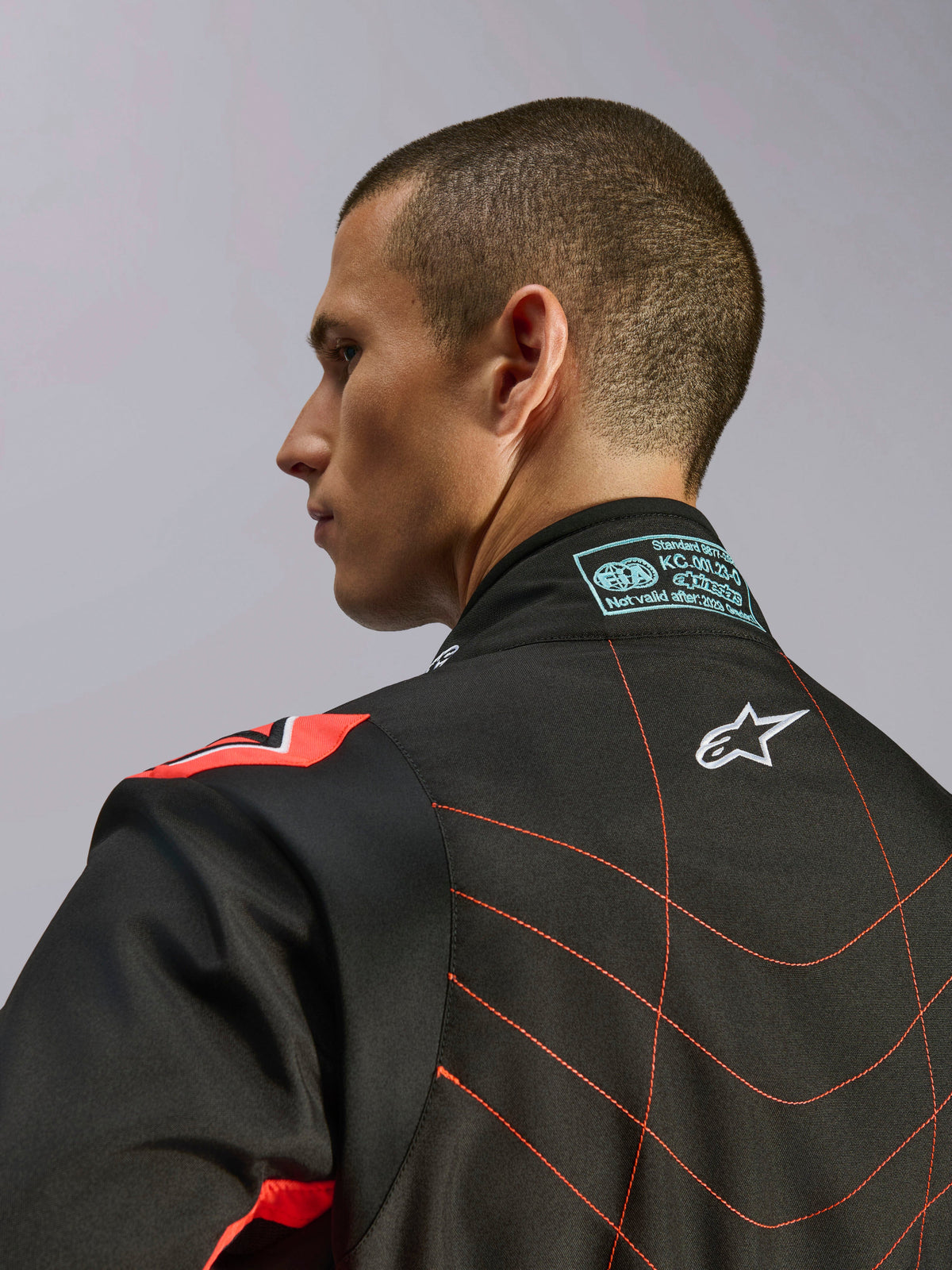 Kombinezon Alpinestars KMX-9 V3, czarno-czerwony fluo kombinezon kartingowy, zbliżenie na górną część pleców i kołnierz na modelu, białe logo Alpinestars, czerwone przeszycia i etykieta certyfikacji FIA na karku