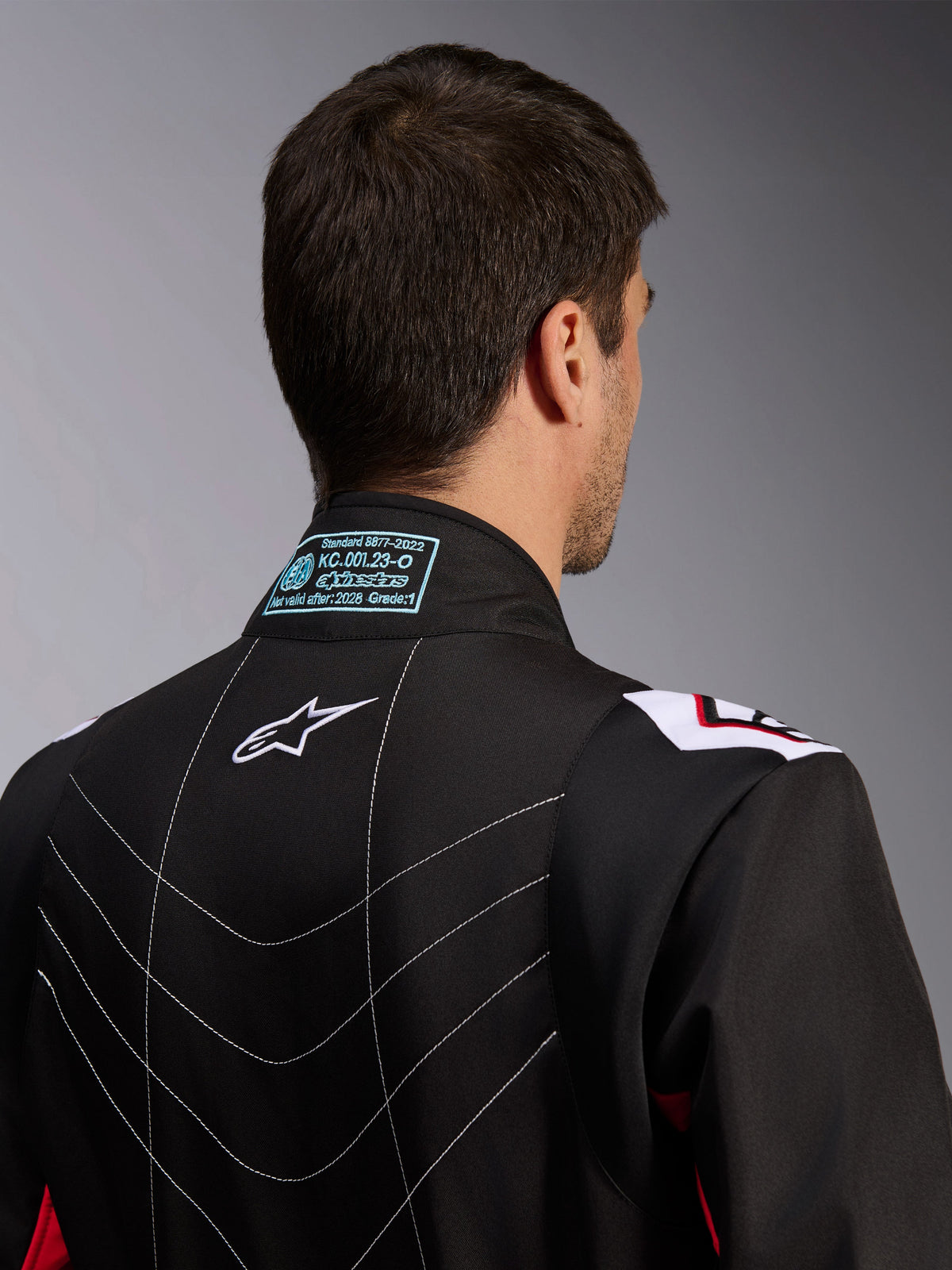 Alpinestars KMX-9 V3 Suit, kombinezon kartingowy, czarno-czerwono-biały, widok kołnierza z tyłu z etykietą homologacji FIA 8877-2022, białym logo Astars i dekoracyjnymi przeszyciami