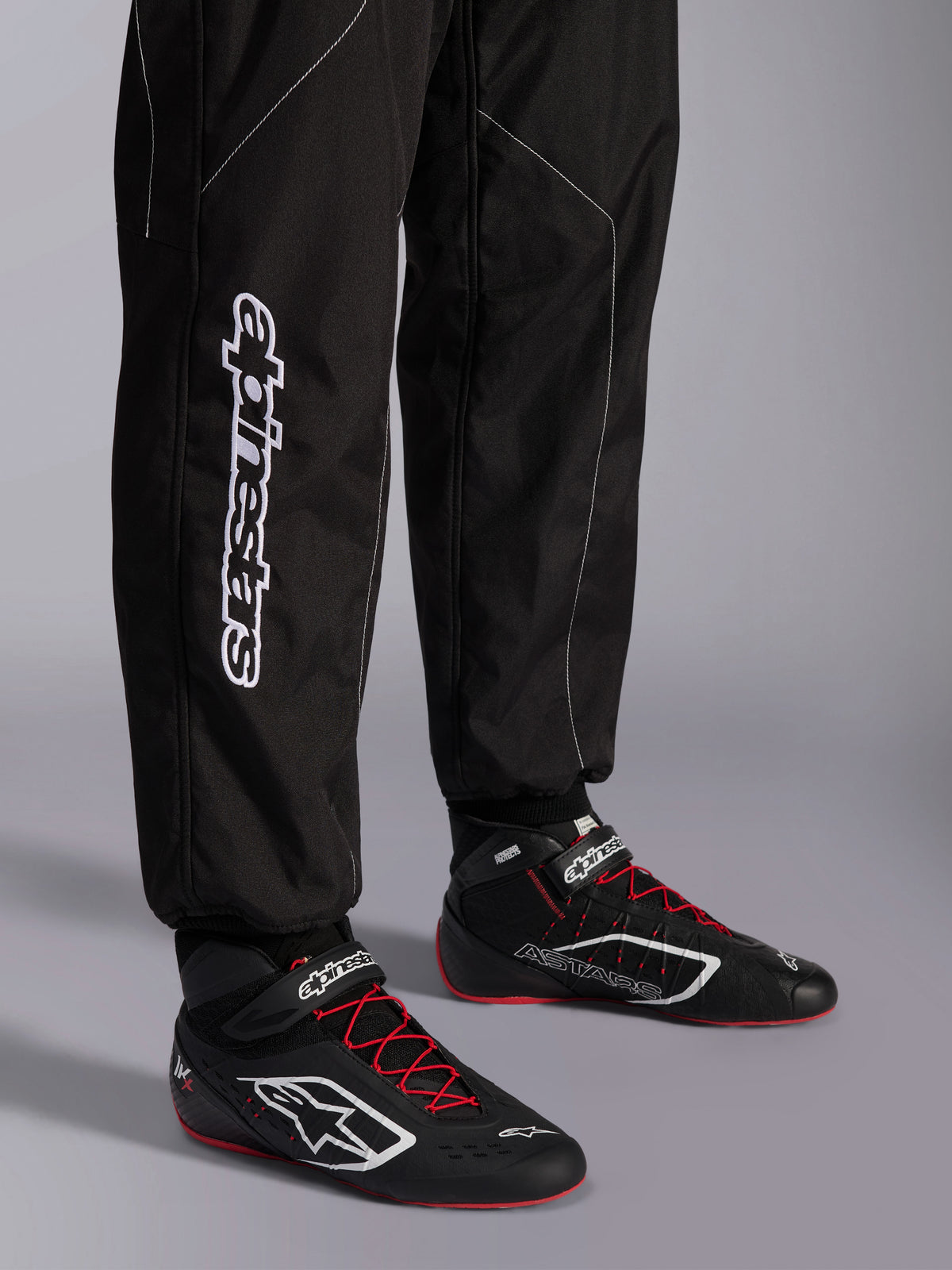 Alpinestars KMX-9 V3 Suit, Karting Suit, Black and White, lower leg view showing large white Alpinestars branding, worn with black and red racing boots, professional motorsport gear for karting