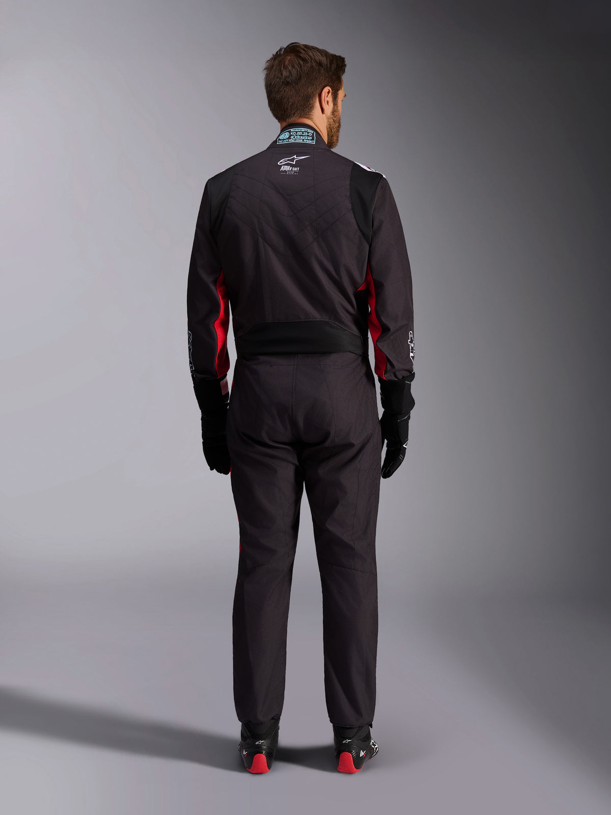 Alpinestars KMX-9 V3 Graphic 3 Suit, kombinezon kartingowy, czarno-czerwony, widok z tyłu przedstawiający elastyczny panel lędźwiowy i metkę z certyfikatem FIA na kołnierzu, zestawiony z czarnymi rękawicami wyścigowymi i butami z czerwonymi akcentami