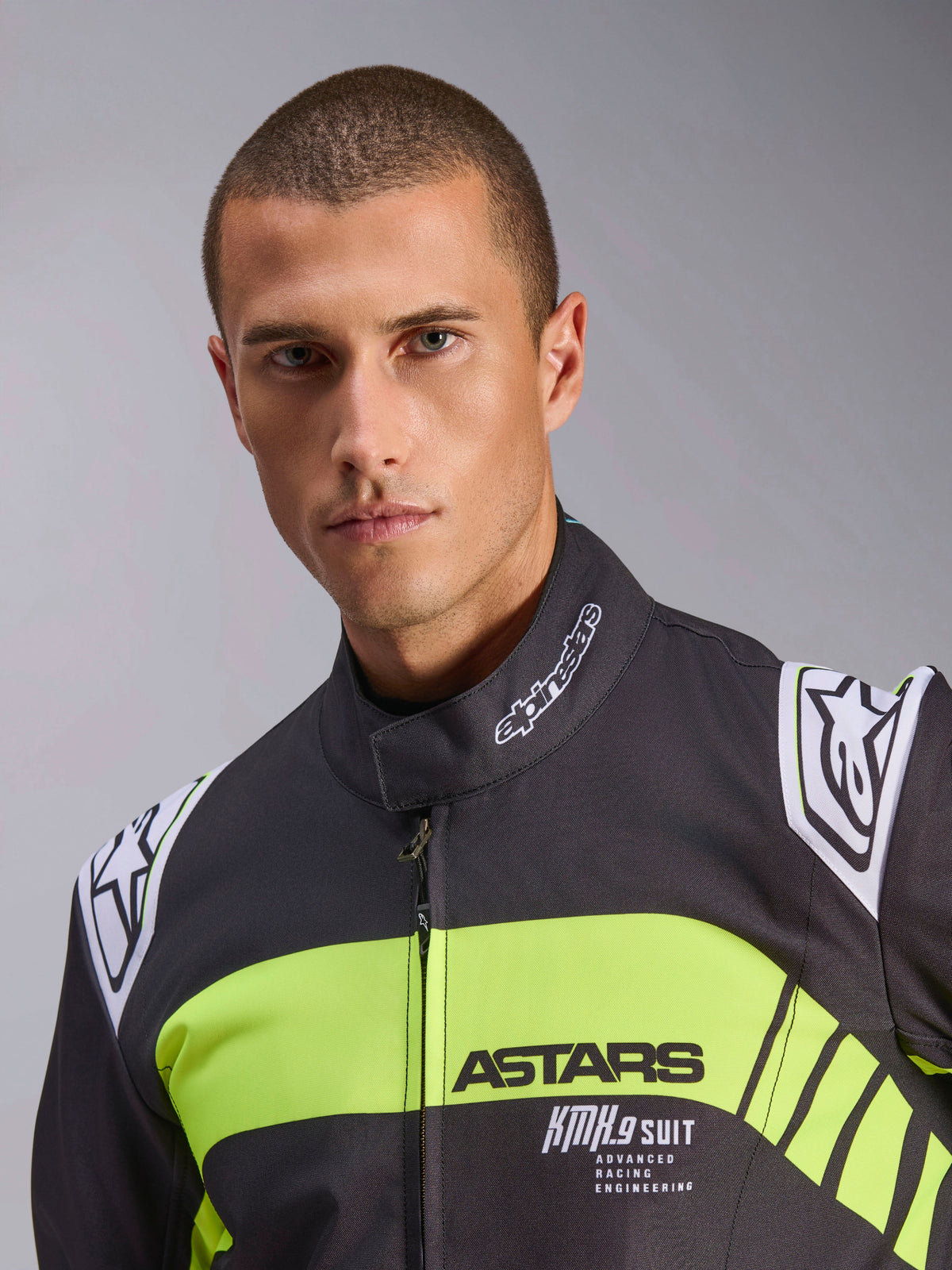 Kombinezon Alpinestars KMX-9 V3 Graphic 3, kombinezon kartingowy, czarny i żółty fluo, zbliżenie portretowe z fluorescencyjnym żółtym pasem na klatce piersiowej z oznaczeniami ASTARS i KMX.9 SUIT, logo Alpinestars na ramionach i kołnierzu, profesjonalna odzież wyścigowa