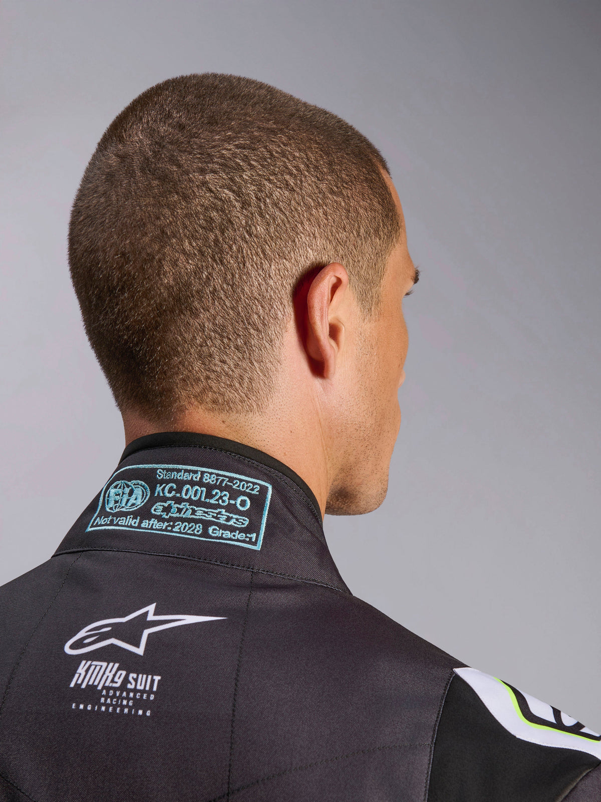 Alpinestars KMX-9 V3 Graphic 3 Suit, zbliżenie na tylną część kołnierza, widoczna etykieta homologacji FIA 8877-2022 Grade 1 oraz białe oznaczenie KMX-9 na czarnym materiale, detal stroju kartingowego