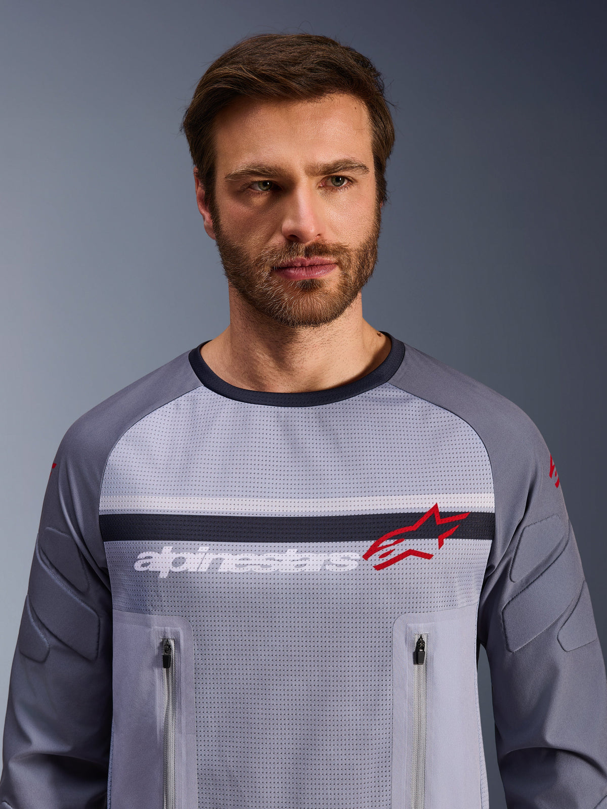 Alpinestars Maxdura Dual Jersey, Mid Gray and Dark Gray, worn by male model, featuring a mesh torso for ventilation, dual zippered chest pockets, white 'alpinestars' branding and red star logo, performance off-road adventure gear