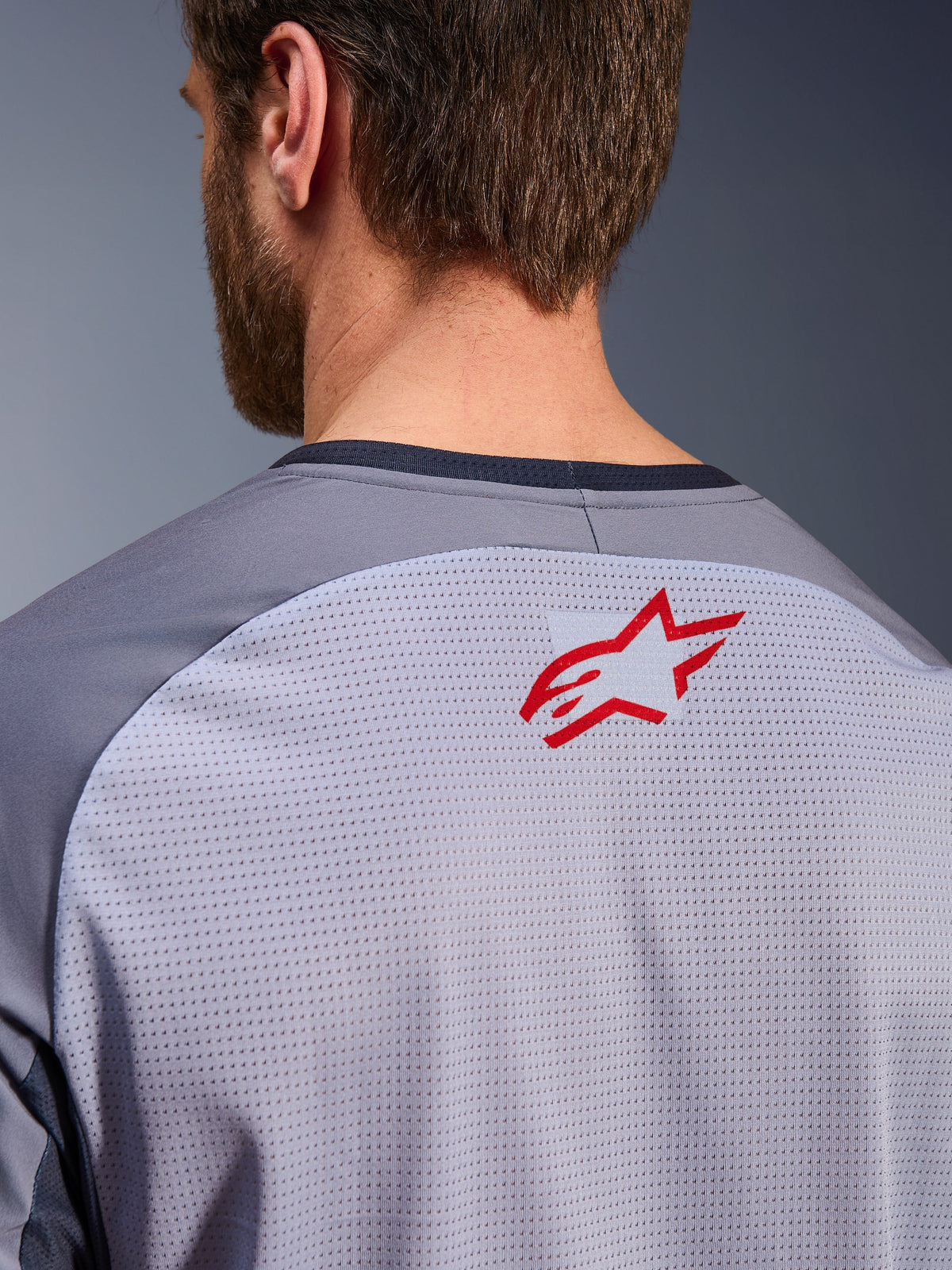 Alpinestars Maxdura Dual Jersey in Mid Gray and Dark Gray, close-up of the upper back and collar, features a small red Alpinestars star logo on breathable light gray mesh fabric with dark gray neck trim, designed for adventure off-road riding