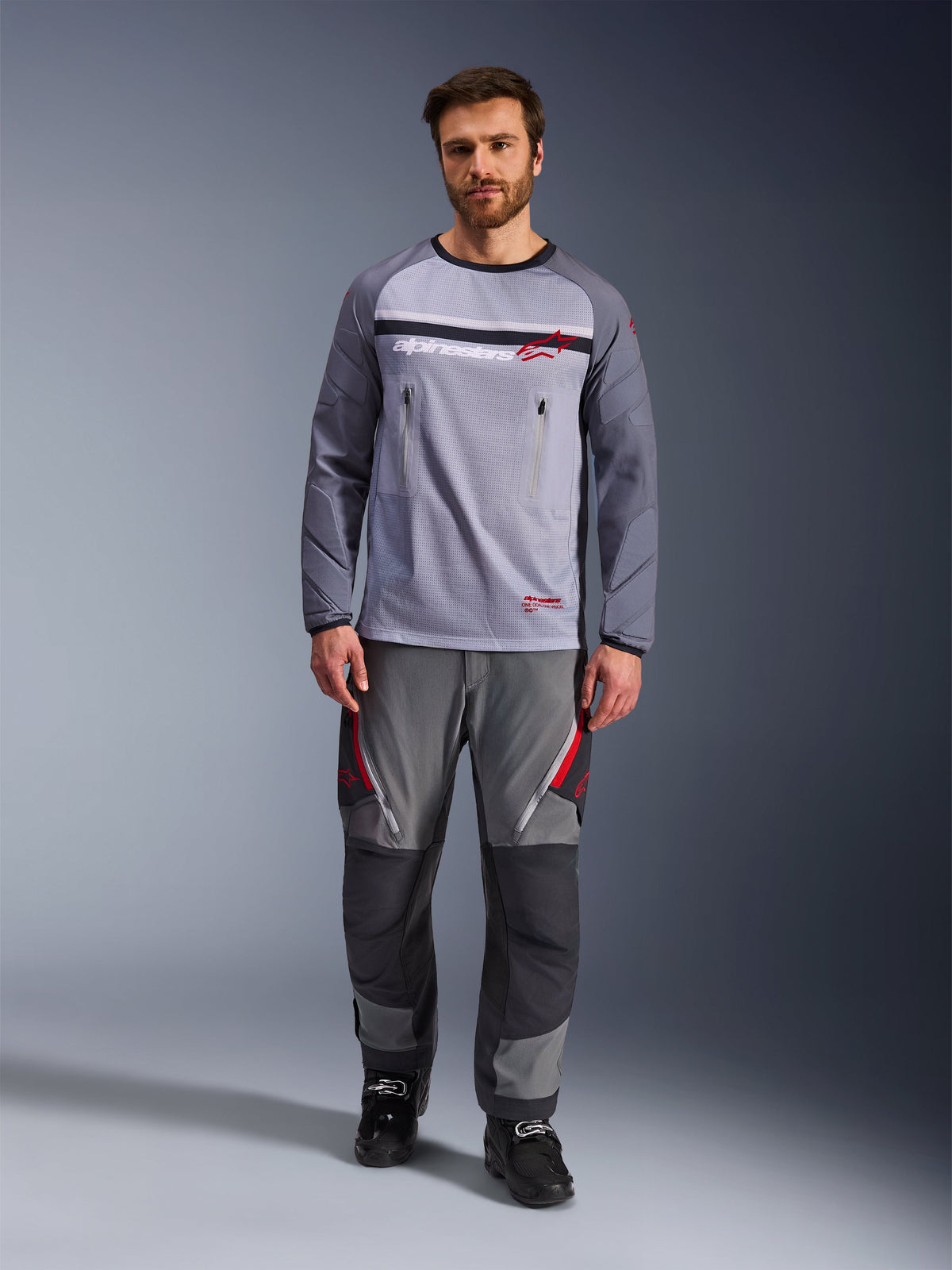 Alpinestars Maxdura Dual Jersey, Mid Gray and Dark Gray, adventure motorcycle jersey with mesh torso and zippered chest pockets, abrasion-resistant sleeves with integrated padding, worn with matching gray performance pants with red accents, technical off-road riding gear