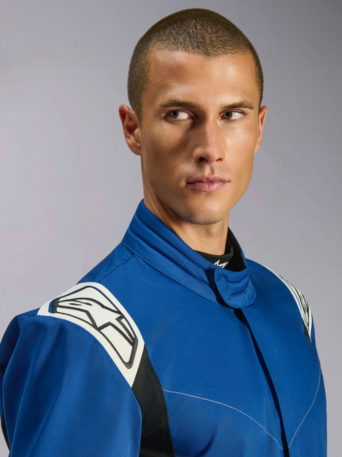 Kombinezon Alpinestars Kart Indoor V2, niebieski kombinezon kartingowy, zbliżenie na modela, białe panele na ramionach z czarnym logo gwiazdy, ergonomiczny kołnierz, wytrzymały jednowarstwowy materiał o splocie skośnym do wyścigów rekreacyjnych