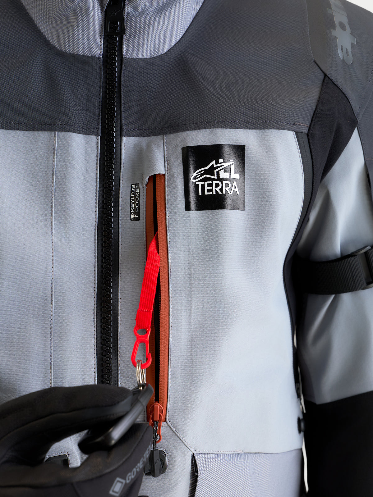 Alpinestars St-7 V2 2L Gore-Tex kurtka motocyklowa adventure, szara i czarna, zbliżenie na wodoodporną kieszeń keyless z czerwonym sznurkiem mocującym i brandingiem All Terra