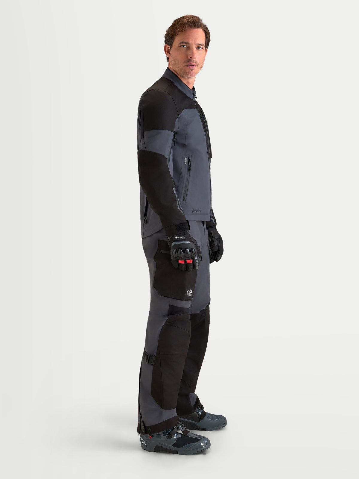 Alpinestars Arenis Gore-Tex Jacket, men's adventure touring motorcycle jacket in black and deep gray, side profile view showing waterproof textile construction and ergonomic collar worn by a model.