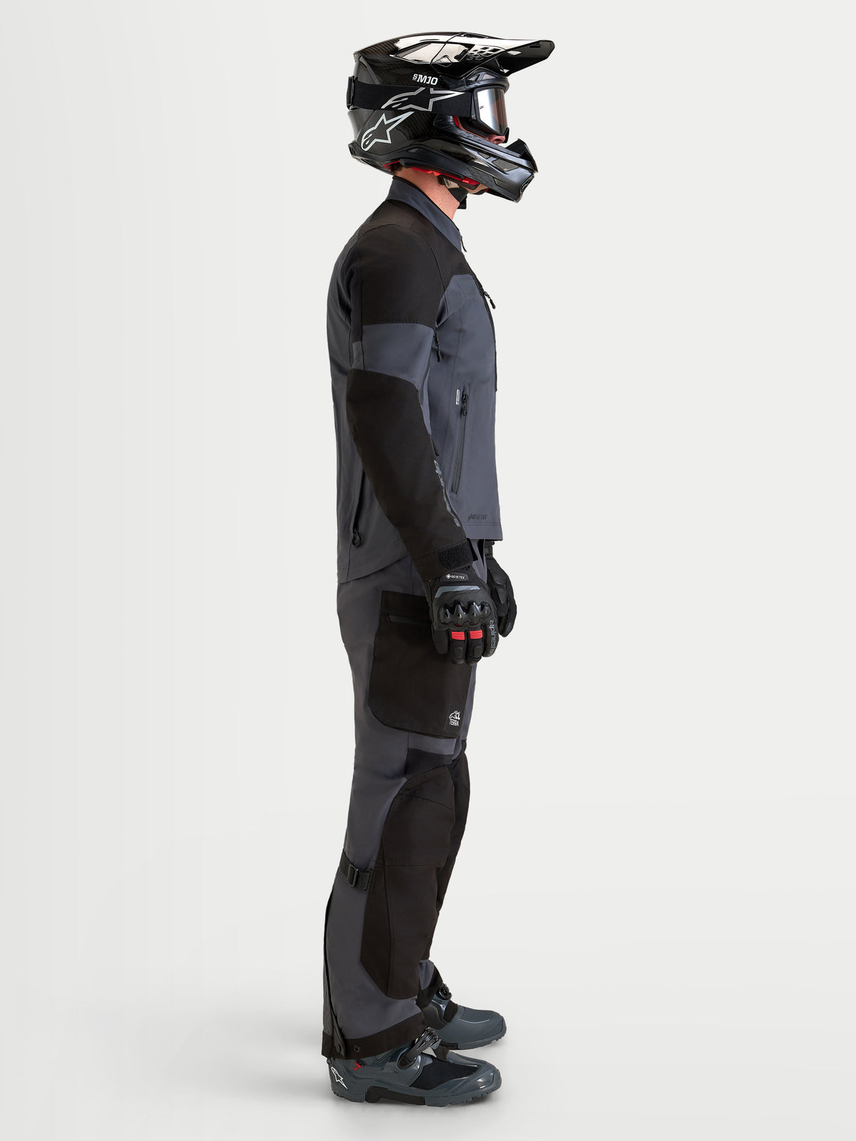 Alpinestars Arenis Gore-Tex Jacket, men's adventure touring motorcycle textile jacket in black and deep gray, side profile view on a model wearing matching gear and helmet, AA certified waterproof all-terrain riding apparel.