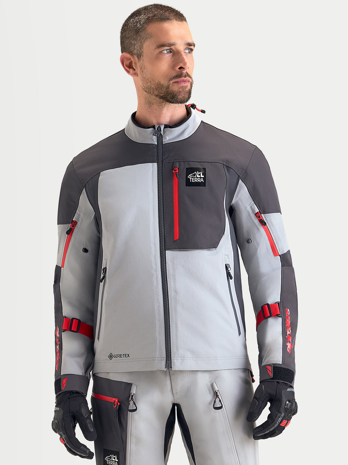 Alpinestars Arenis Gore-Tex kurtka motocyklowa adventure męska w kolorze jasnoszarym, ciemnoszarym i czarnym, widok z przodu na modelu prezentującym wodoodporną konstrukcję tekstylną i zapinaną na zamek kieszeń na piersi