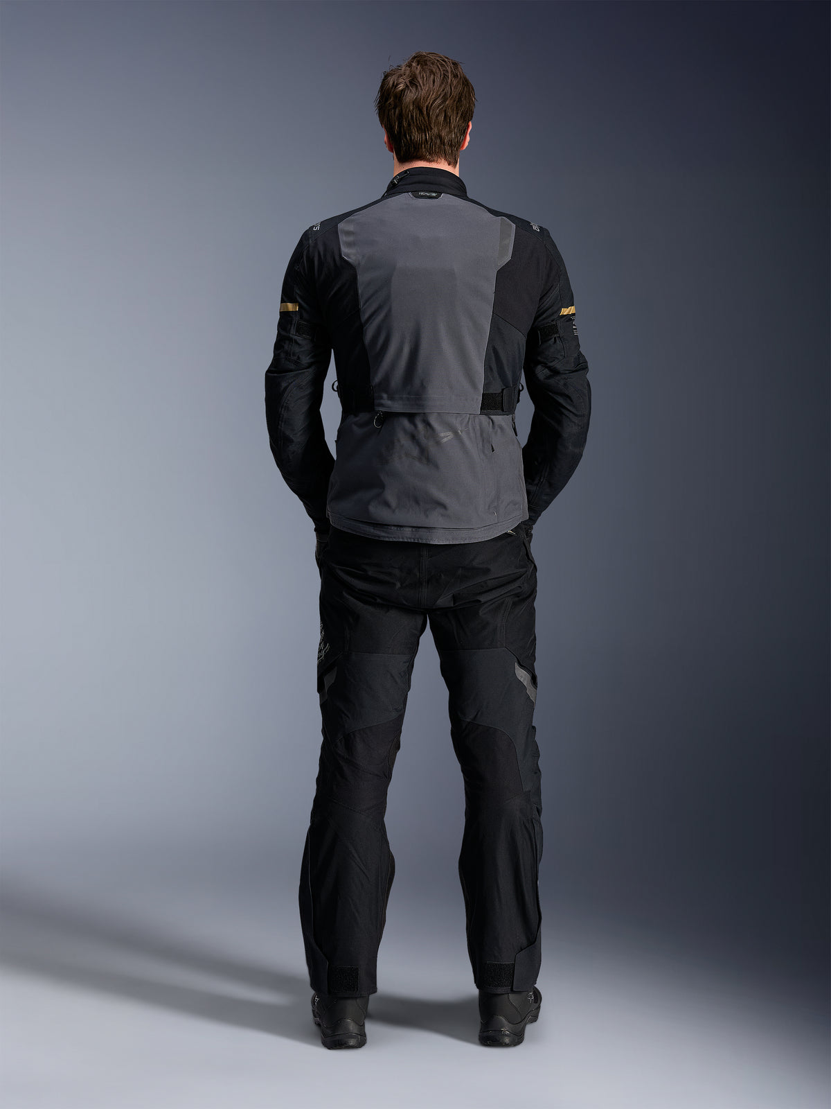 Kurtka Alpinestars ST-7 2L GORE-TEX, Deep Gray Black i Dark Khaki, widok z tyłu na modelu, motocyklowa kurtka turystyczna typu adventure z szarym panelem tylnym i czarnymi profilowanymi rękawami, noszona z pasującymi czarnymi spodniami.