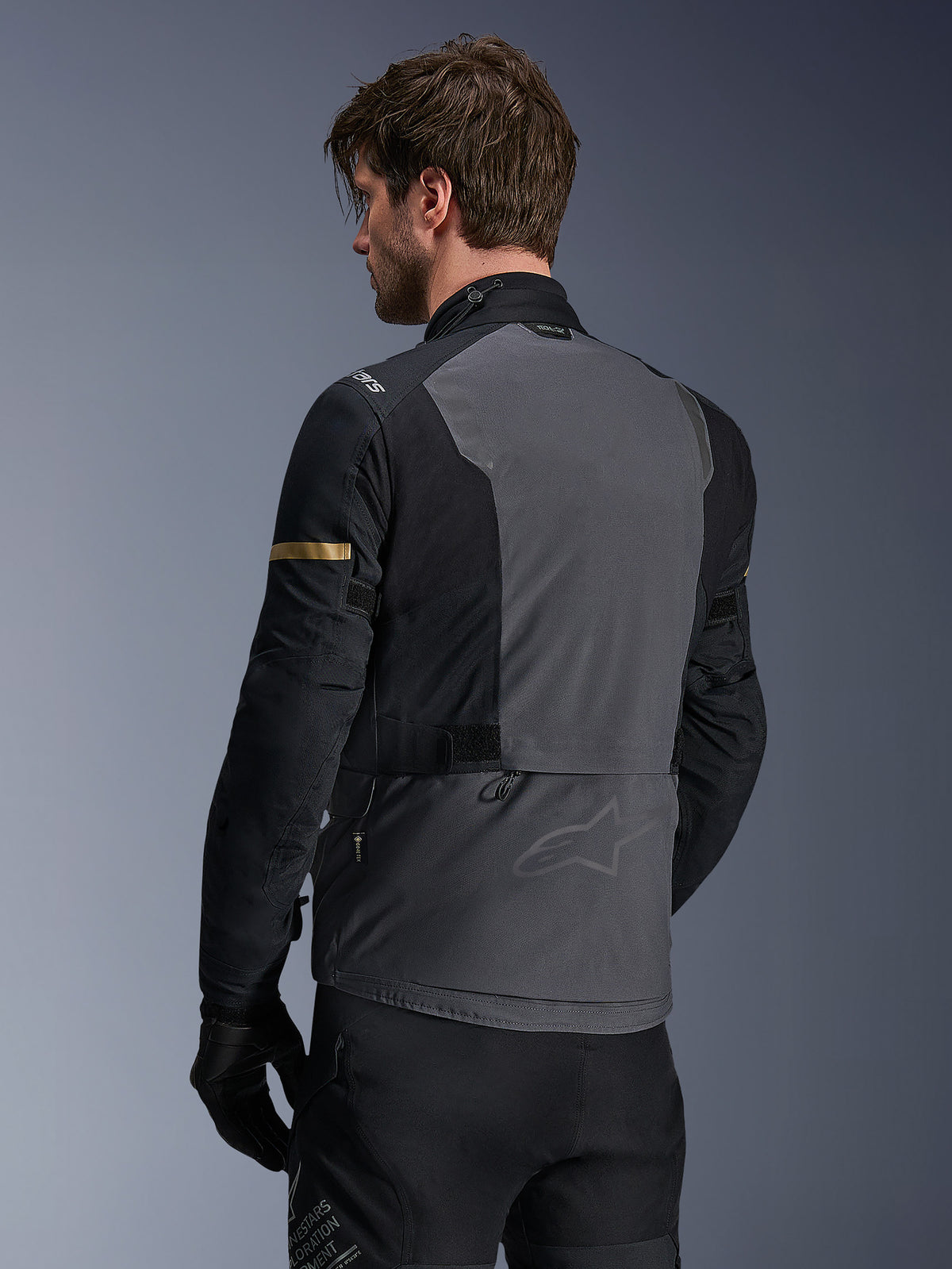 Kurtka Alpinestars ST-7 2L GORE-TEX, kurtka motocyklowa, Deep Gray Black i Dark Khaki, widok z tyłu ukazujący duży szary panel na plecach z subtelnym brandingiem, czarne rękawy ze złotymi akcentami khaki, wodoodporna konstrukcja tekstylna typu adventure