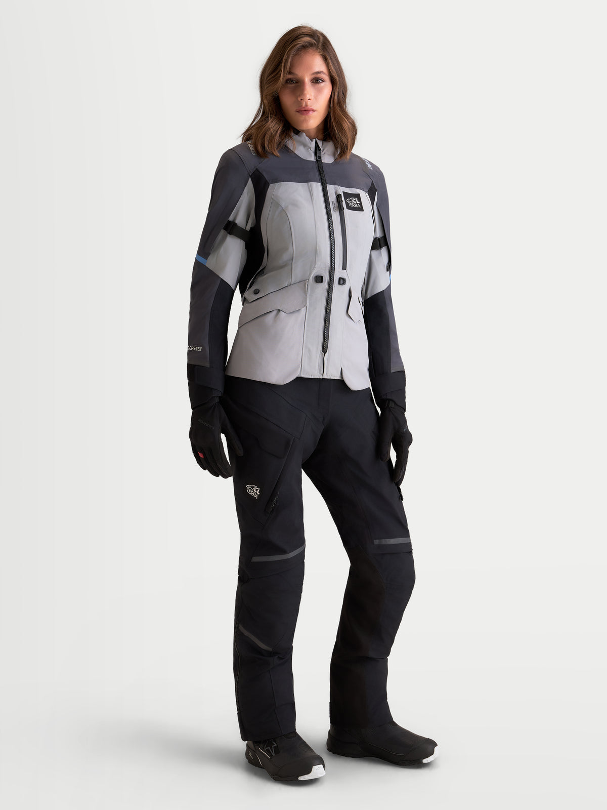 Alpinestars Stella St-7 V2 2L Gore-Tex kurtka motocyklowa damska adventure w kolorze szarym, ciemnoszarym i czarnym, widok z przodu na modelce w pasujących spodniach, butach i rękawicach, wodoodporna konstrukcja tekstylna