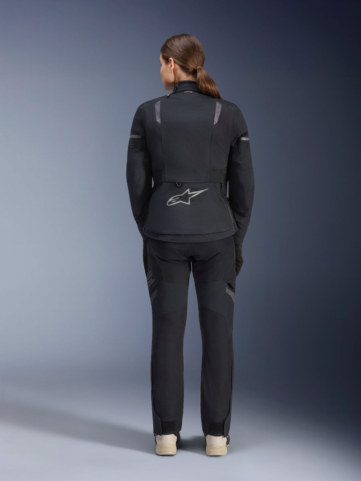 Damska kurtka Alpinestars Stella ST-7 2L GORE-TEX, czarno-ciemnoszara, widok z tyłu ze srebrnym logo Alpinestars na dole pleców, zestawiona z pasującymi czarnymi spodniami tekstylnymi, motocyklowa odzież turystyczna adventure