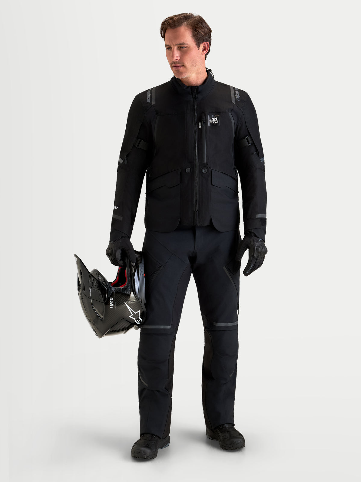 Alpinestars ST-7 V2 2L Gore-Tex spodnie motocyklowe adventure męskie, czarne, widok z przodu na model w pasującym sprzęcie trzymający kask, wodoodporna odzież turystyczna z certyfikatem AA