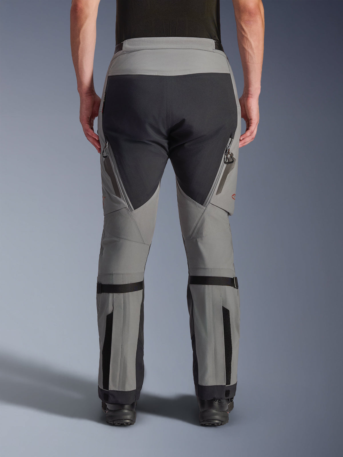 Spodnie Alpinestars Nazca 3L GORE-TEX PRO, motocyklowe spodnie adventure, ciemnoszare i czarne, widok z tyłu, wyposażone w zapinane na zamek wyloty wentylacyjne na udach, regulatory objętości łydek i wzmocnione panele na siedzeniu, zaprojektowane do ekstremalnej jazdy w terenie.