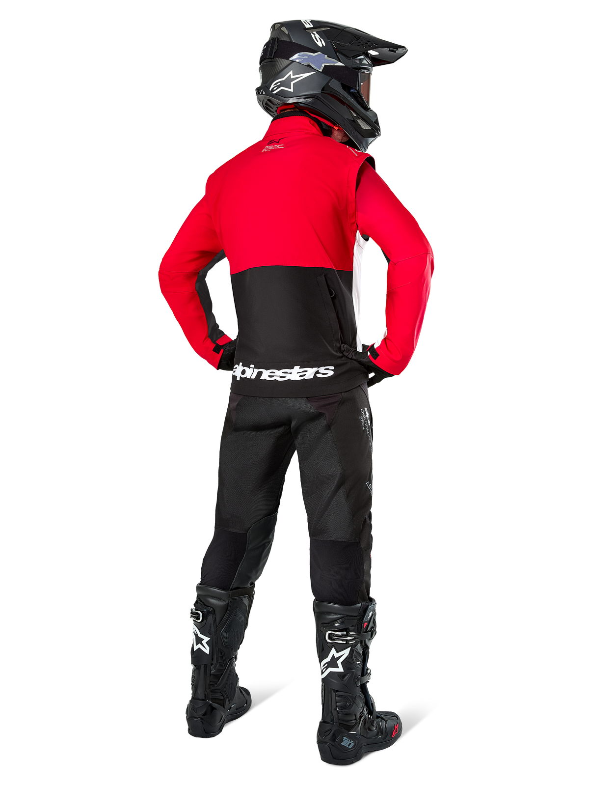 Motocross rider seen from behind wearing the Alpinestars Pro-Dura Jacket in Black, Bright Red, and White, paired with black pants, black helmet, and black off-road boots, featuring a red upper and black lower section with white Alpinestars branding across the back.