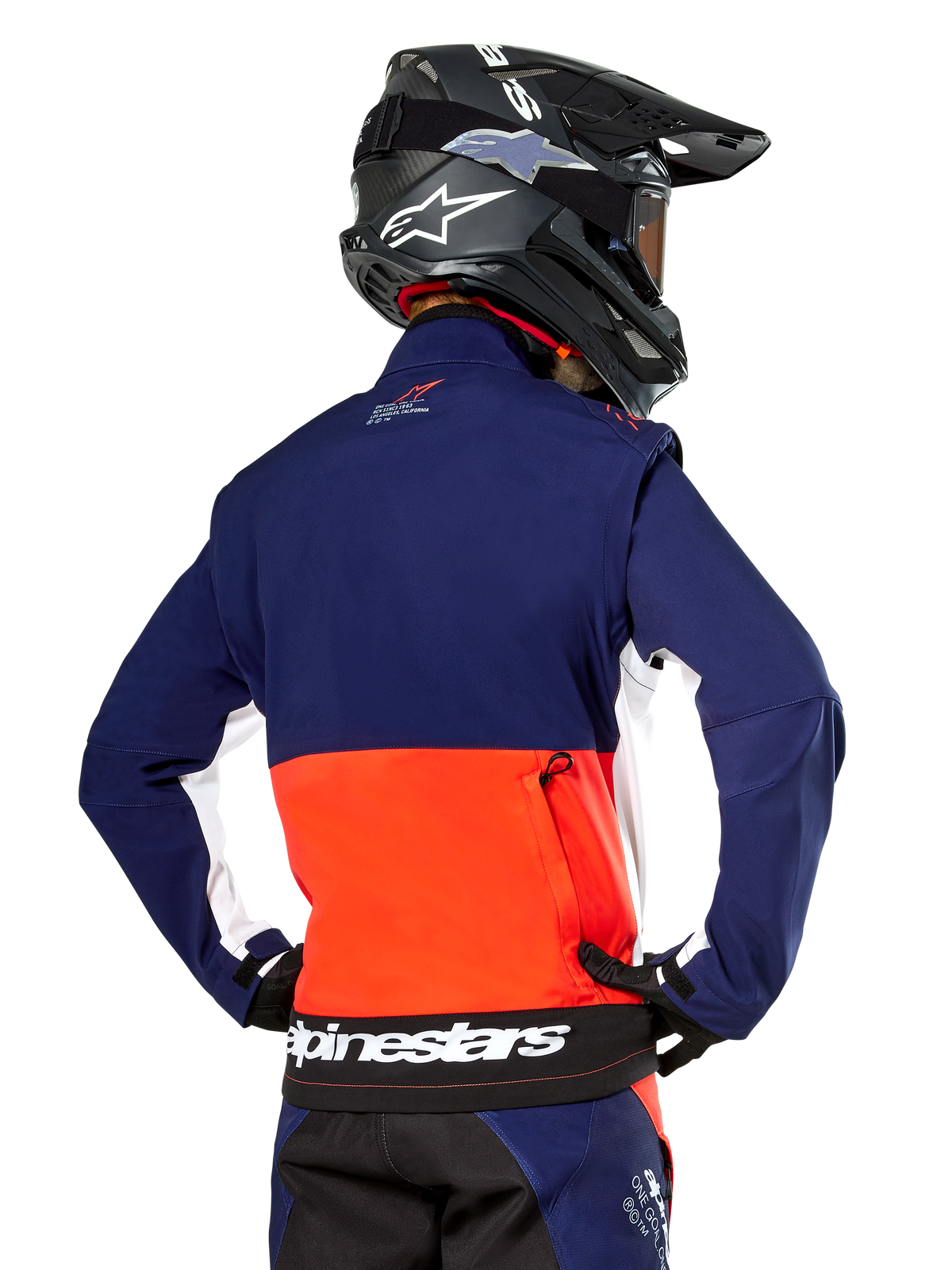 Kurtka Alpinestars Lite-Dura Softshell, granatowa, jaskrawopomarańczowa i biała, widok z tyłu na zawodniku motocrossowym, duże białe logo na dolnej krawędzi, kieszeń na zamek, element kompletnego stroju wyścigowego off-road