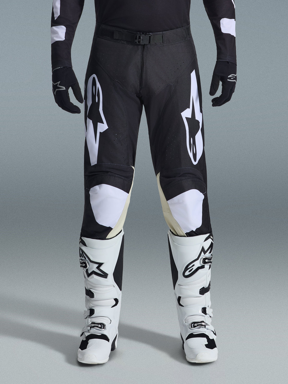 Alpinestars 2026 Racer Air Riway Pants, spodnie motocrossowe, czarno-białe, z wyraźnymi białymi logotypami Alpinestars na udach i panelach kolanowych, w zestawieniu z biało-czarnymi butami motocrossowymi i czarnymi rękawicami, sportowy krój race-fit do jazdy off-road