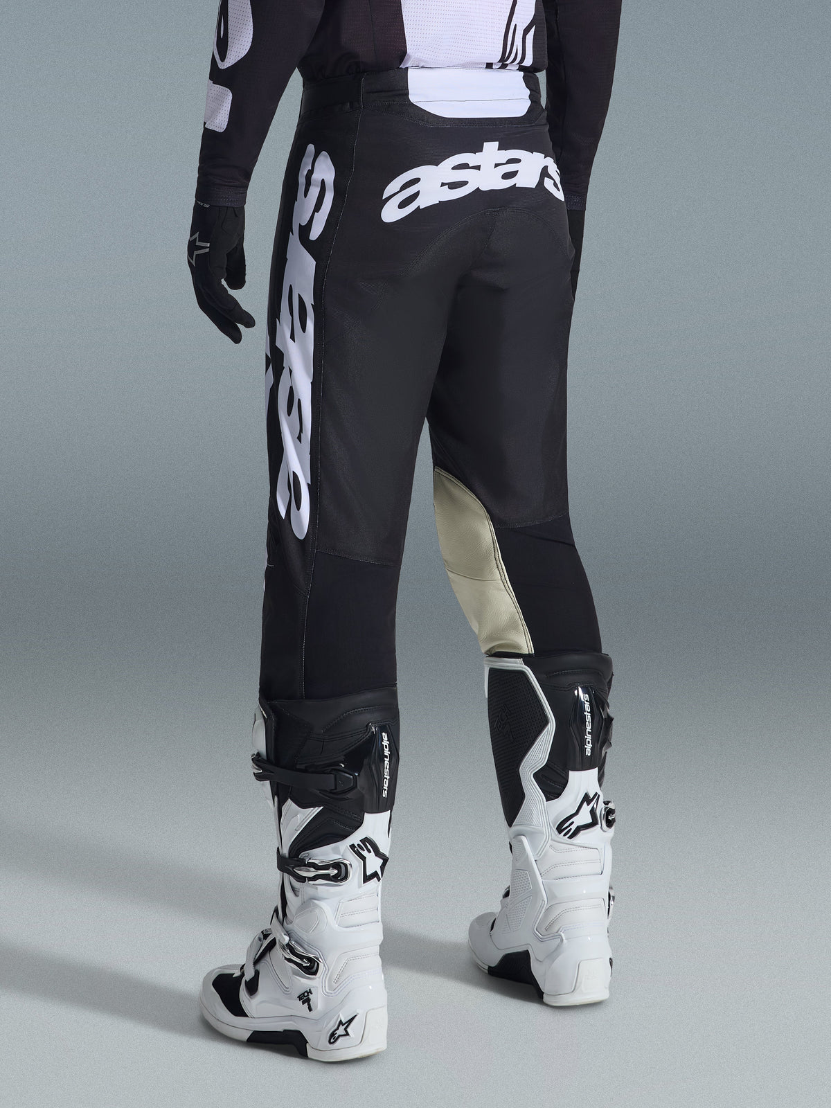 Rear view of Alpinestars 2026 Racer Air Riway Pants in Black and White, featuring prominent white 'astars' branding on the seat and leg, cream leather inner knee panels, worn with matching black and white motocross boots and jersey.