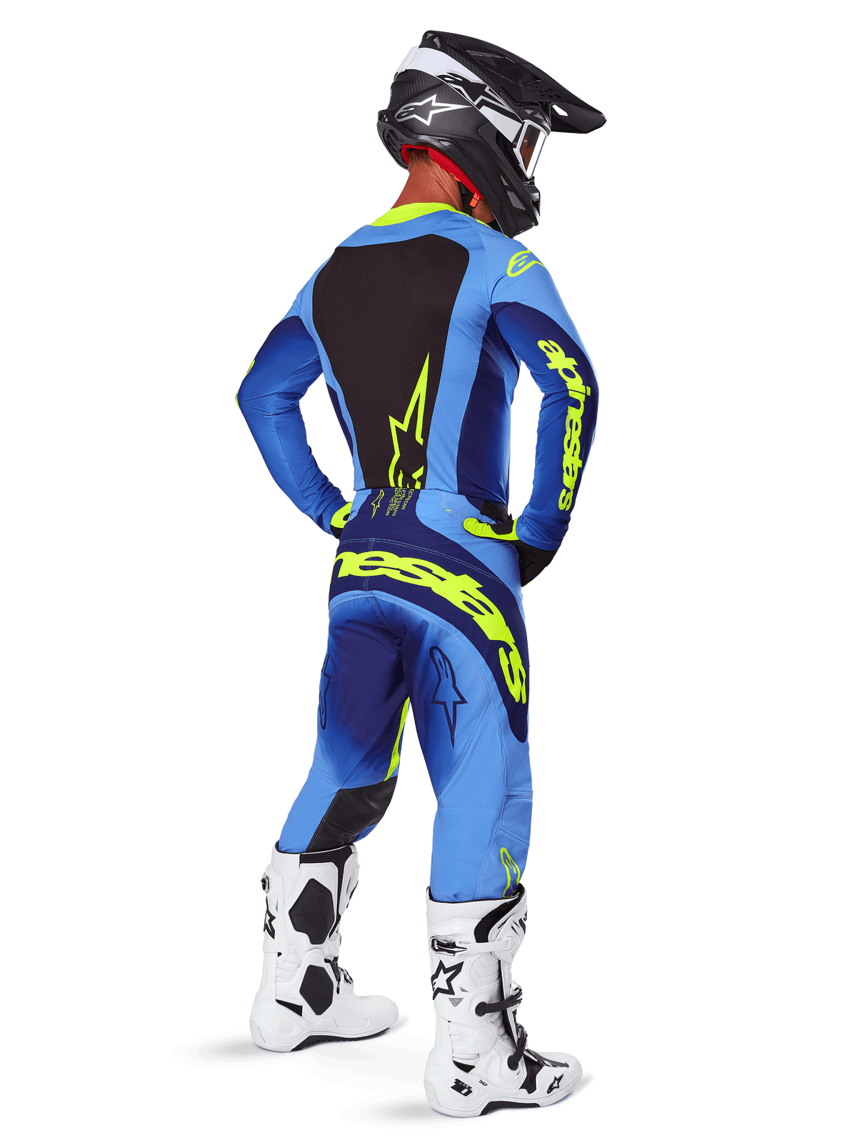 Spodnie Alpinestars Techstar Melt 2025, odzież motocrossowa, żółto-niebieskie (Yellow Fluo Blue), widok z tyłu na motocyklistę w dopasowanej niebieskiej koszulce z dużym żółtym logo, biało-czarne buty i czarny kask, skoordynowany strój wyścigowy do jazdy off-road