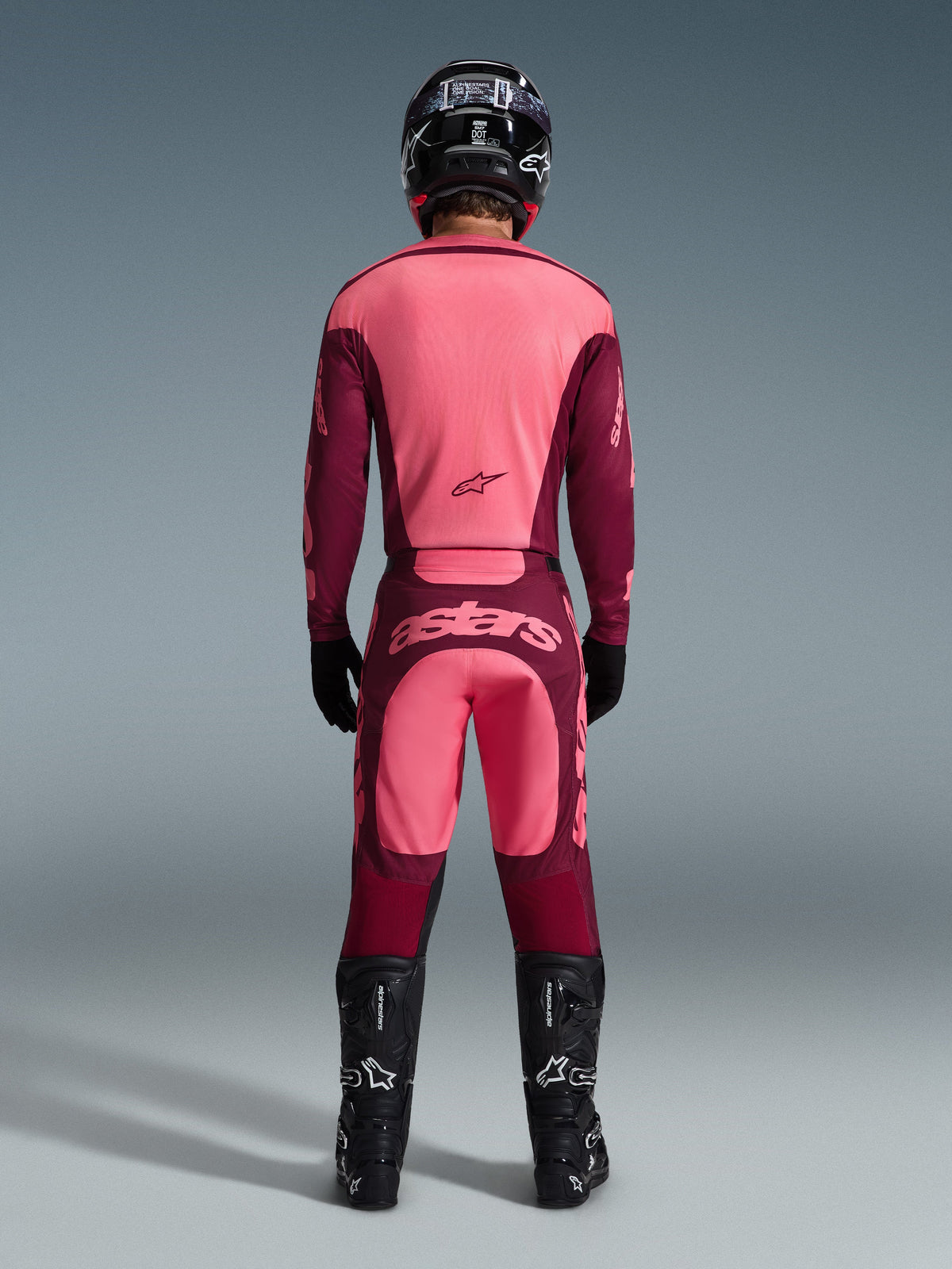 Motocross rider from the back wearing Alpinestars 2026 Racer Riway Pants in Dark Red Coral, matching jersey, black helmet, black gloves, and black Alpinestars boots, featuring a bold 'astars' logo on the seat and a two-tone red design.